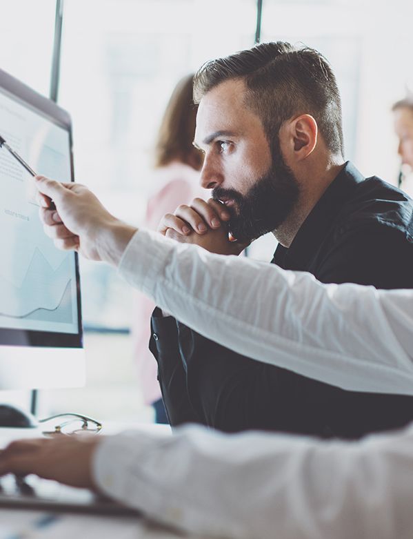 two men are sitting at a desk looking at a computer screen .