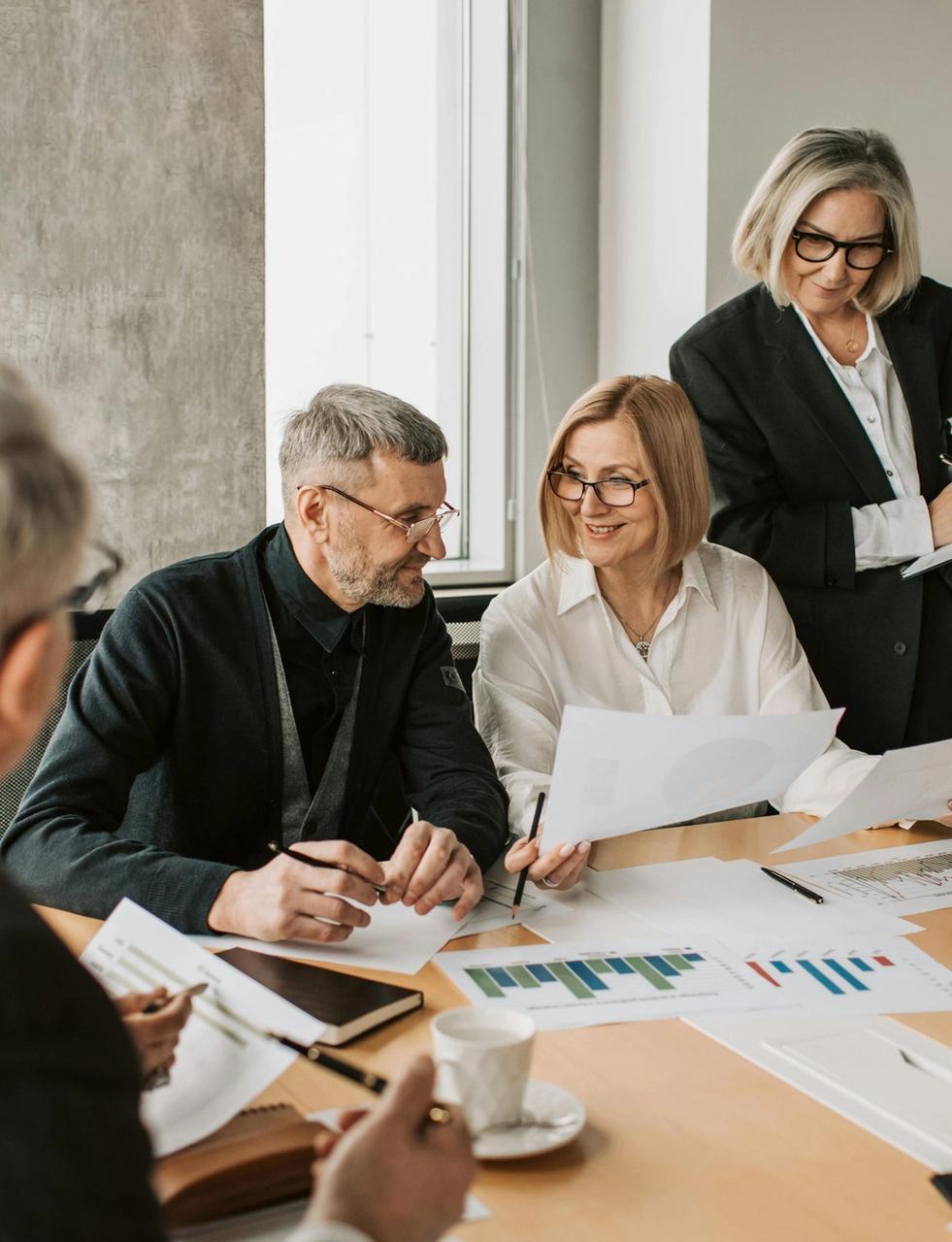 Senior business professionals review documents and charts at a conference table.