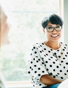 a woman in a polka dot shirt is sitting at a table talking to another woman .