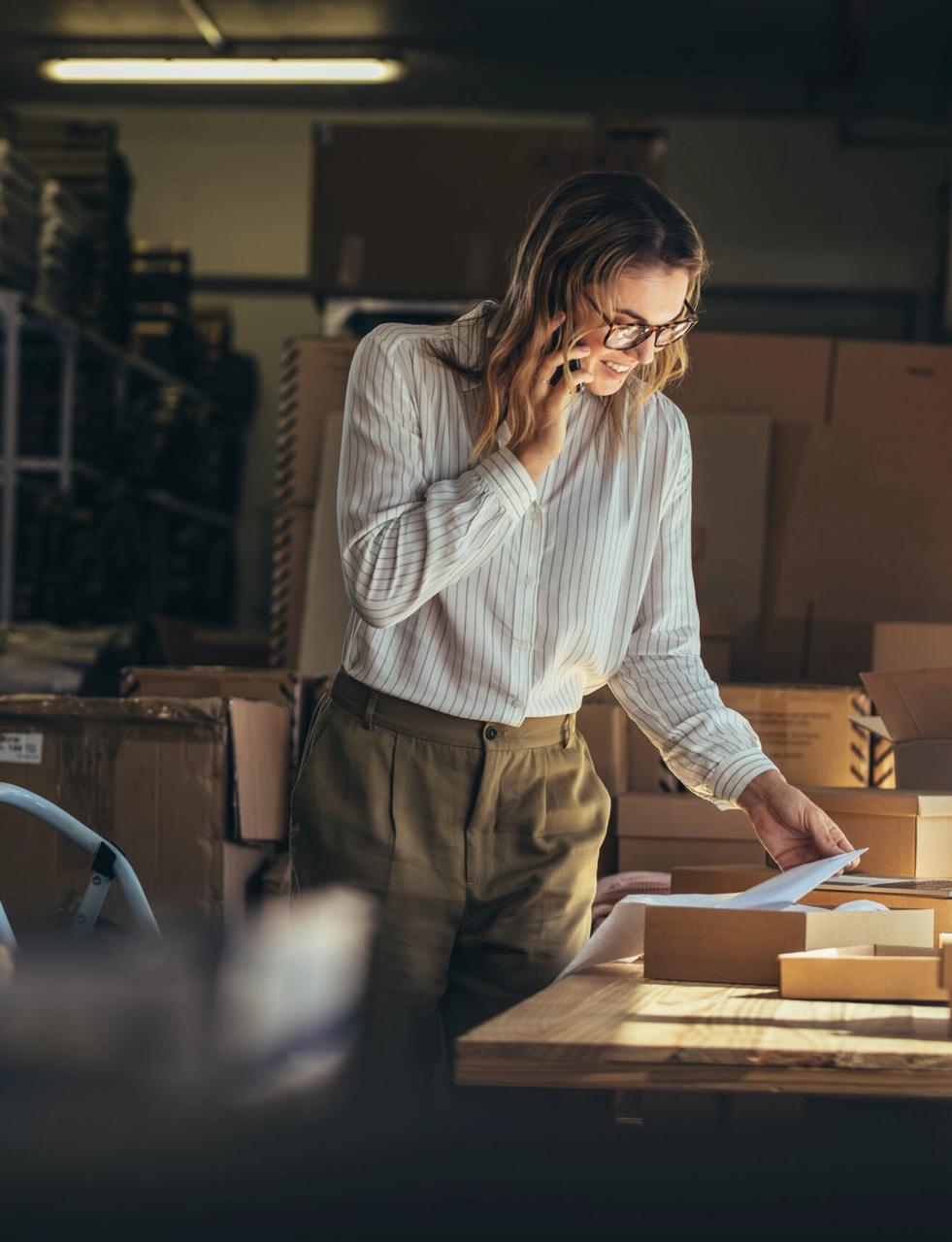 a woman is talking on a cell phone in a warehouse while looking at a piece of paper .