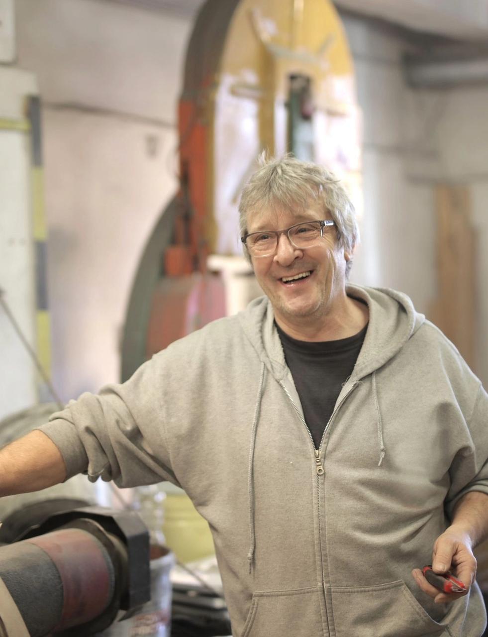 a man is smiling while leaning on a machine in a workshop .