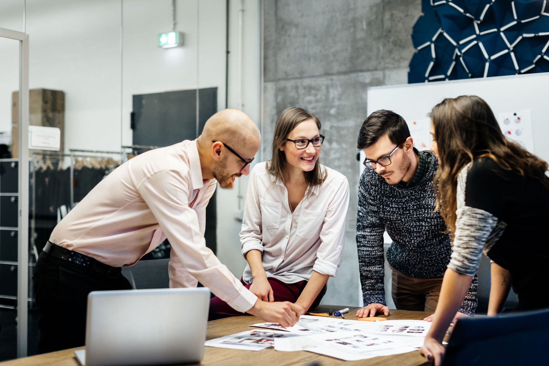 a group of people are standing around a table looking at a laptop .