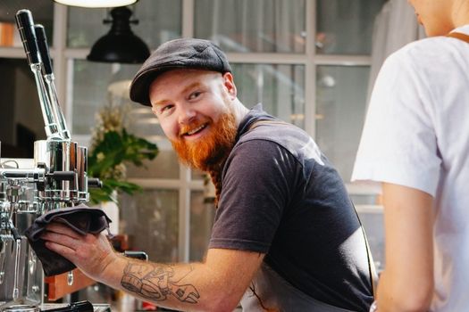 a man with a beard is cleaning a coffee machine in a cafe .