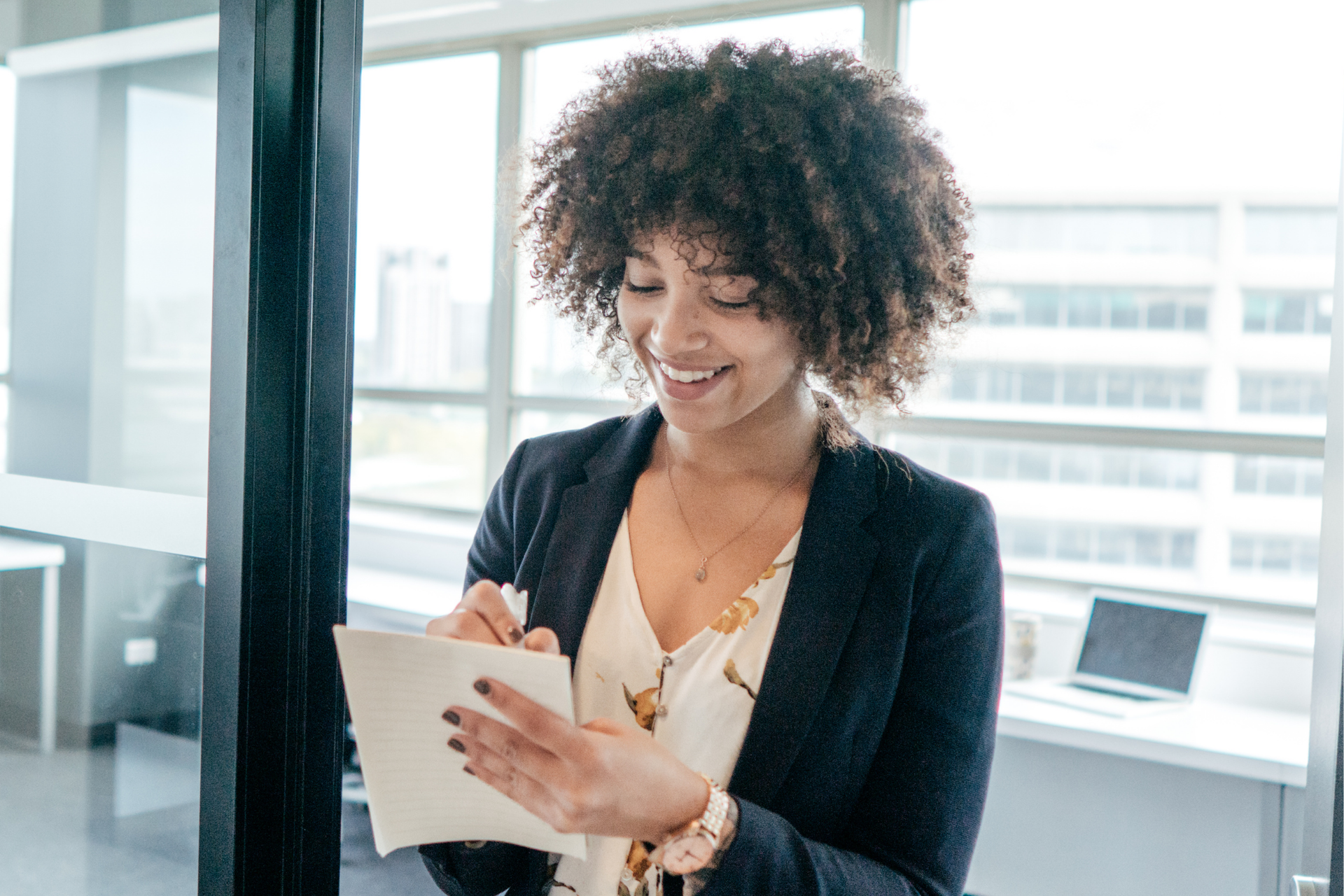 Smiling woman with curly hair writing notes in an office.