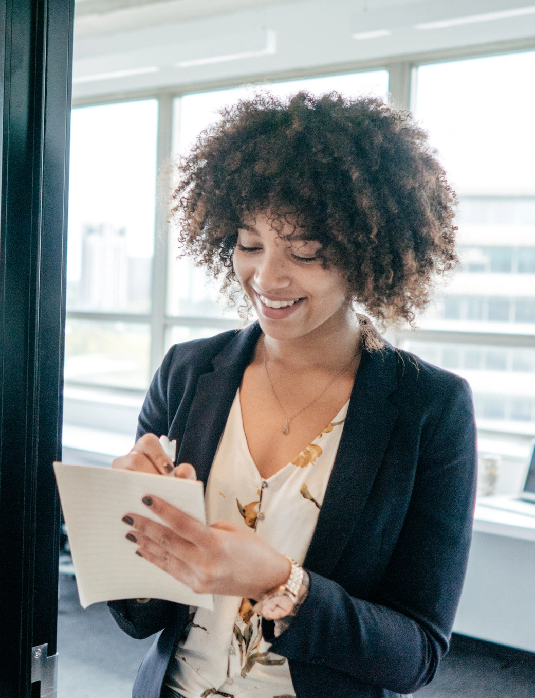 Smiling woman with curly hair writing notes in an office.