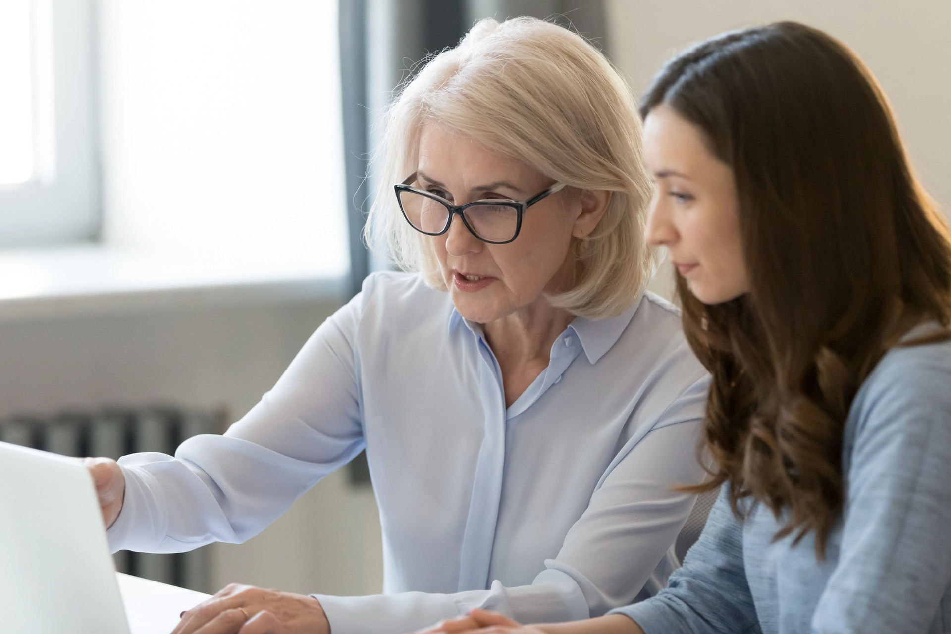 An older woman points to a laptop screen while a younger woman observes.