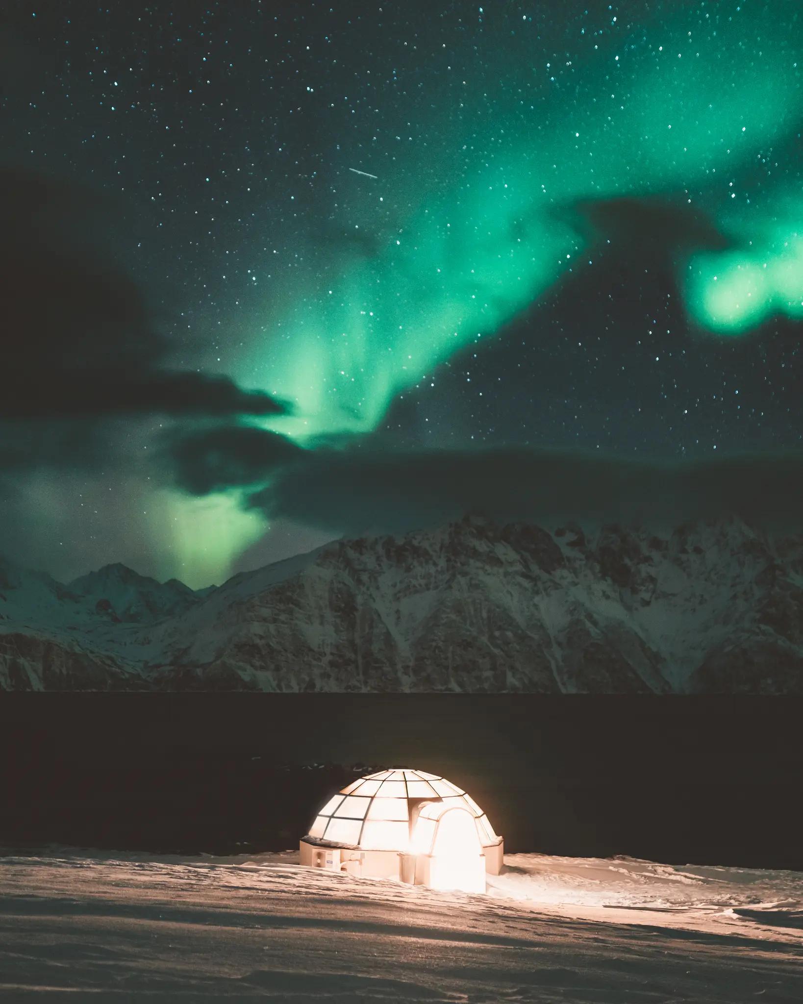 360º Glass igloo seen from the outside at Lyngen North with the Lyngen Alps in the background and the northern lights above