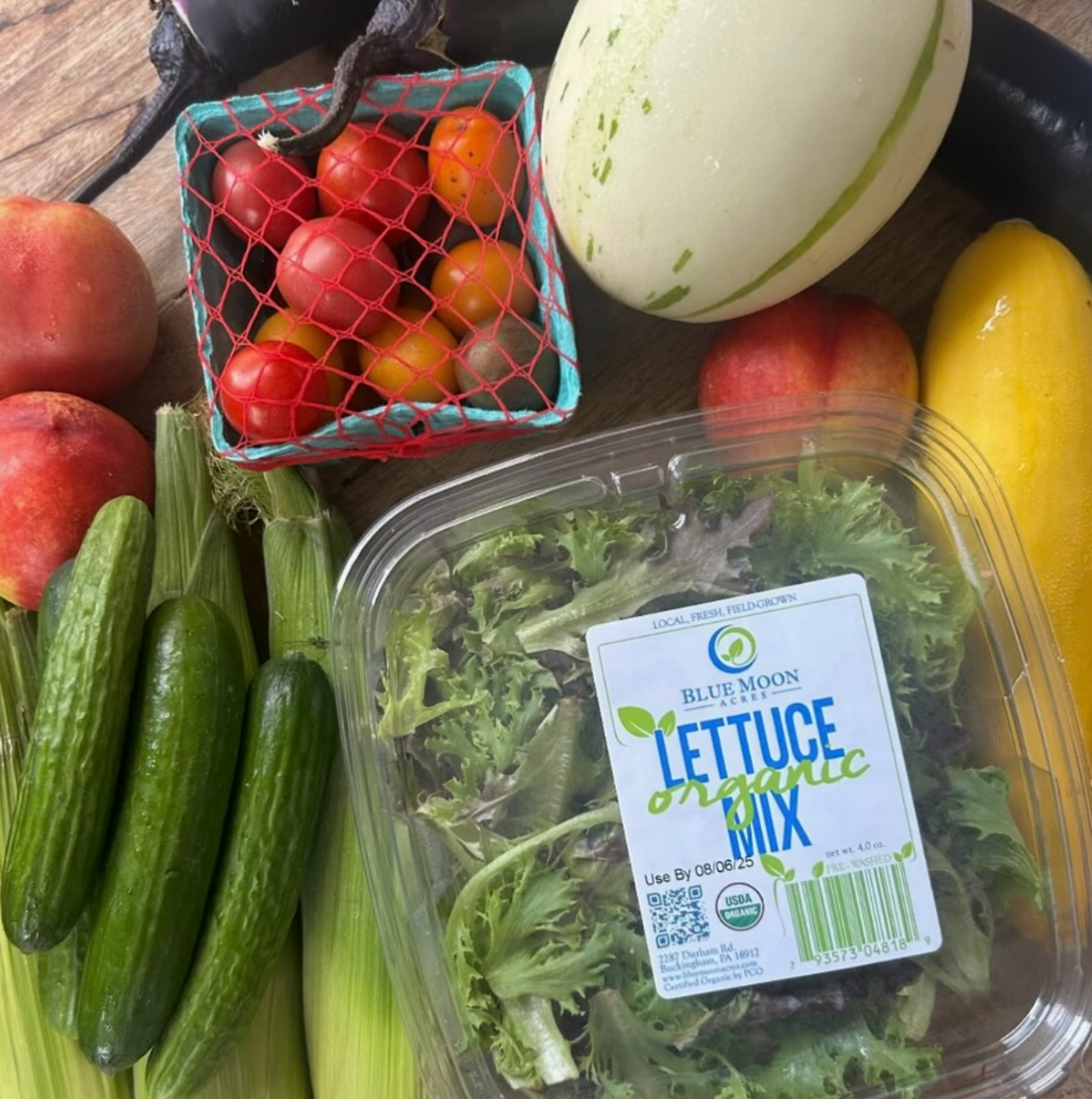 A spread of produce including tomatoes, cucumbers, lettuce, squash, and apricots.
