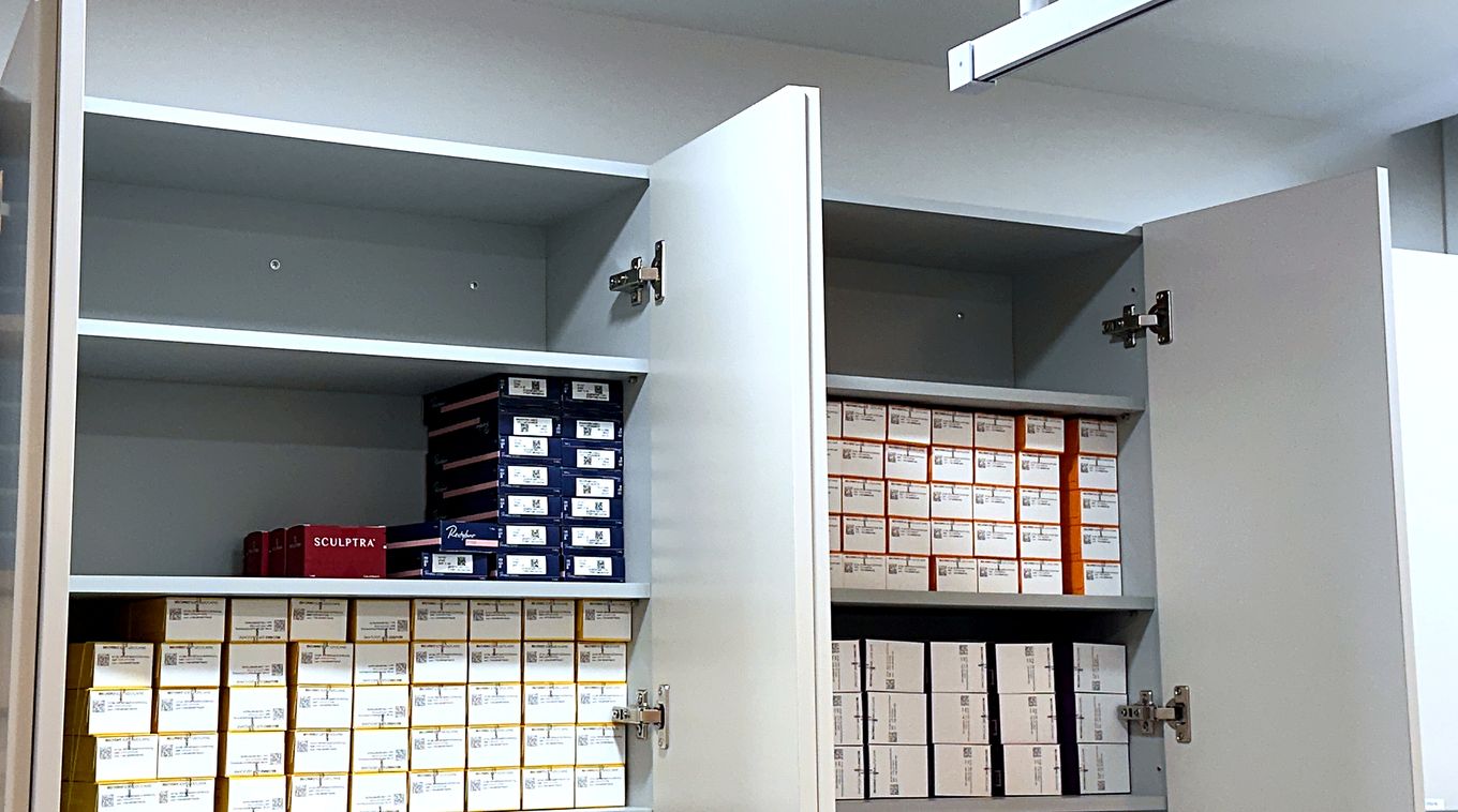 Sculptra, Restylane and Belotero filler boxes lined up in the clinic storage cabinet with QR labels facing out