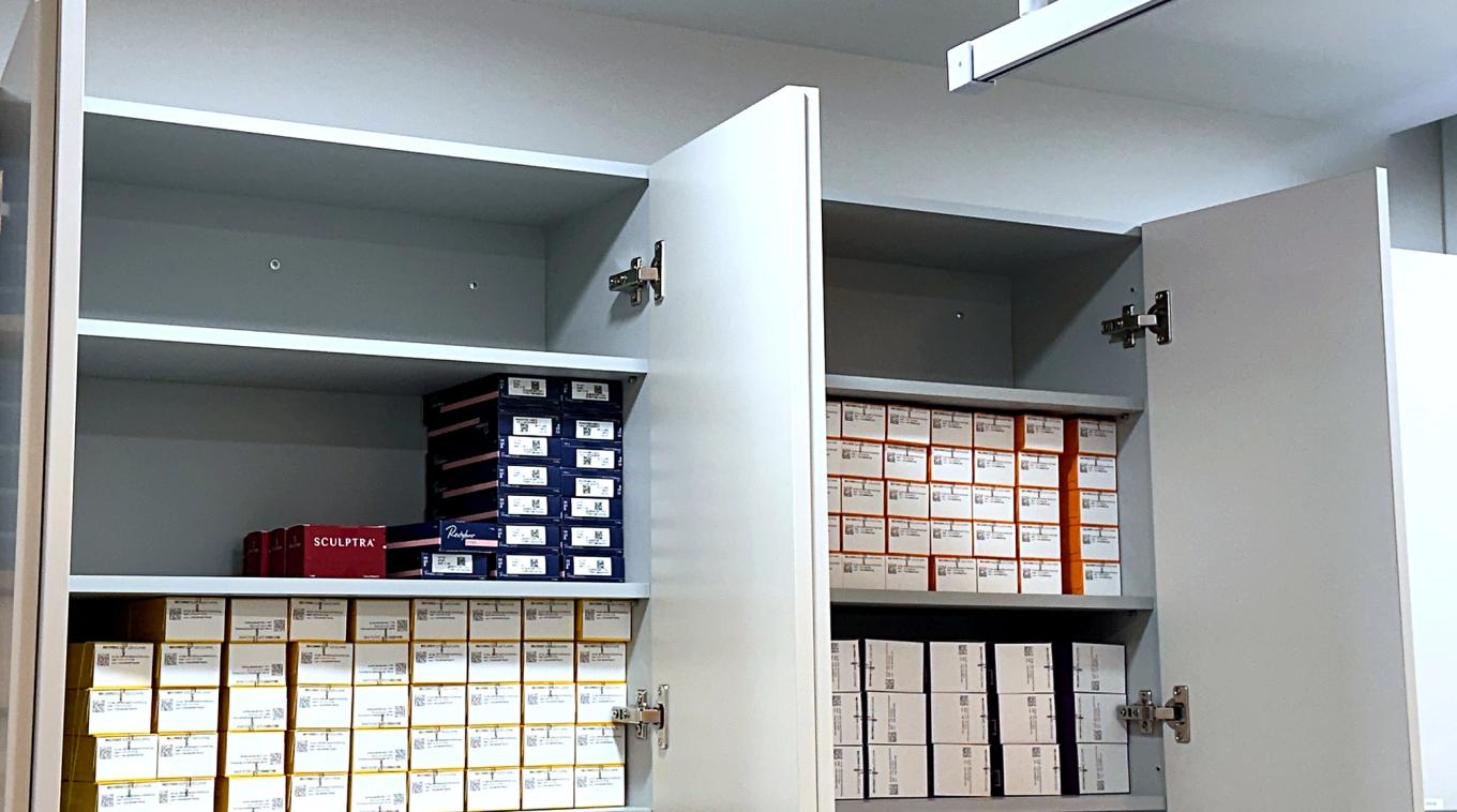 Sculptra, Restylane and Belotero filler boxes lined up in the clinic storage cabinet with QR labels facing out