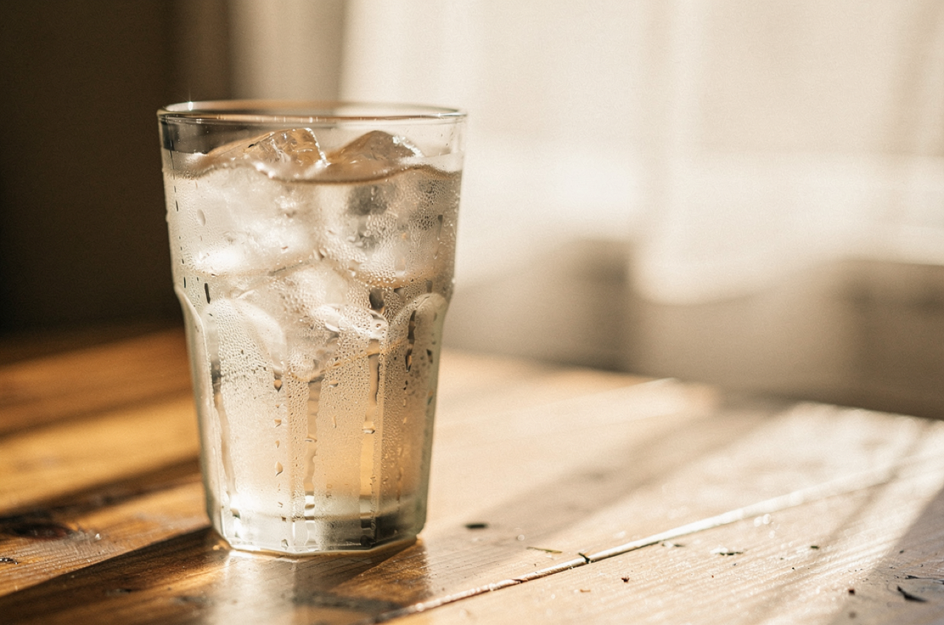 Summer mood photo of a glass of cold water with condensation on a sunlit table