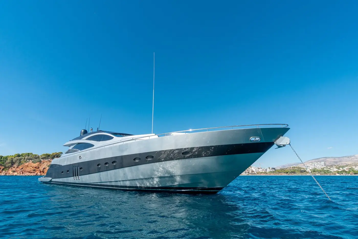 M/Y ONE, a 27 metre Pershing 90 of the George Yachts list, at anchor off the Athens Riviera with the coast behind her; she boards at Flisvos marina, Athens