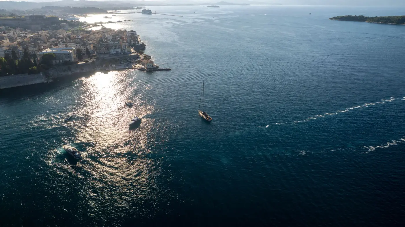 Aerial view of yachts approaching the old town and fortress of Corfu in late afternoon light, Greek waters