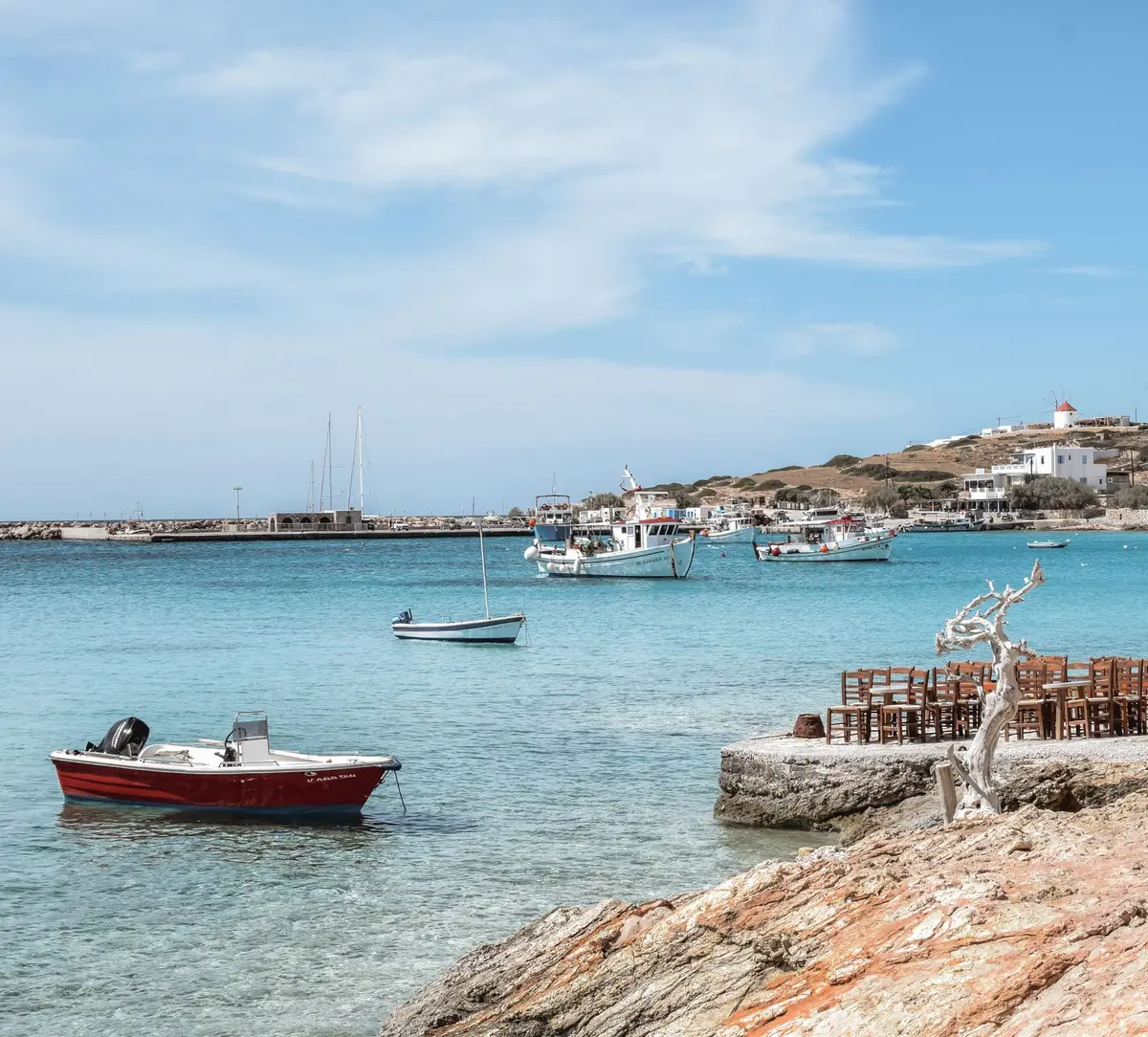 Fishing boats and a tender at anchor in the clear shallow water of Koufonisia in the Small Cyclades, with a windmill on the hill above.