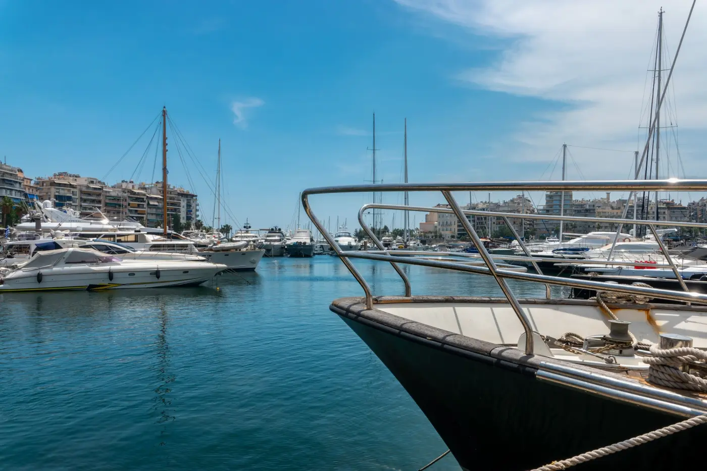 Crewed yachts moored in an Athens marina with the city behind, the departure point for most Greek charter weeks