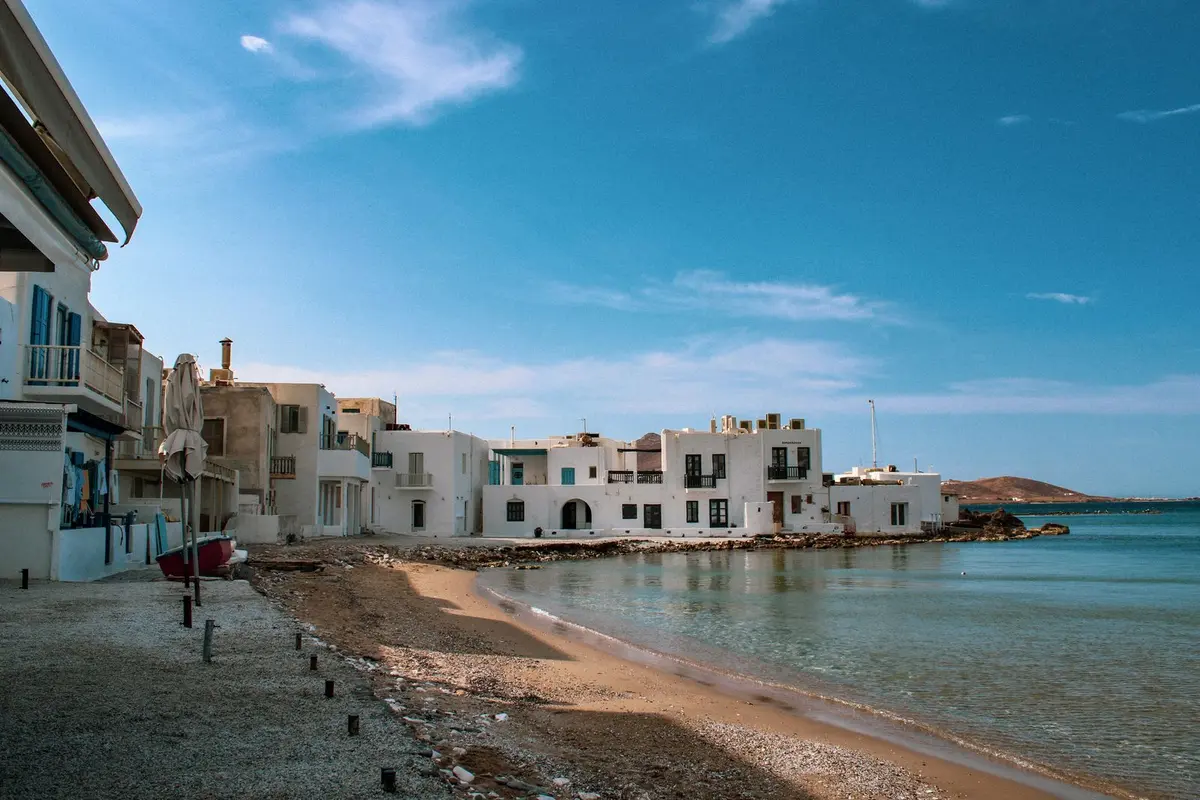 The waterfront at Naoussa on Paros, whitewashed houses on the shore of a shallow turquoise bay in the Cyclades.
