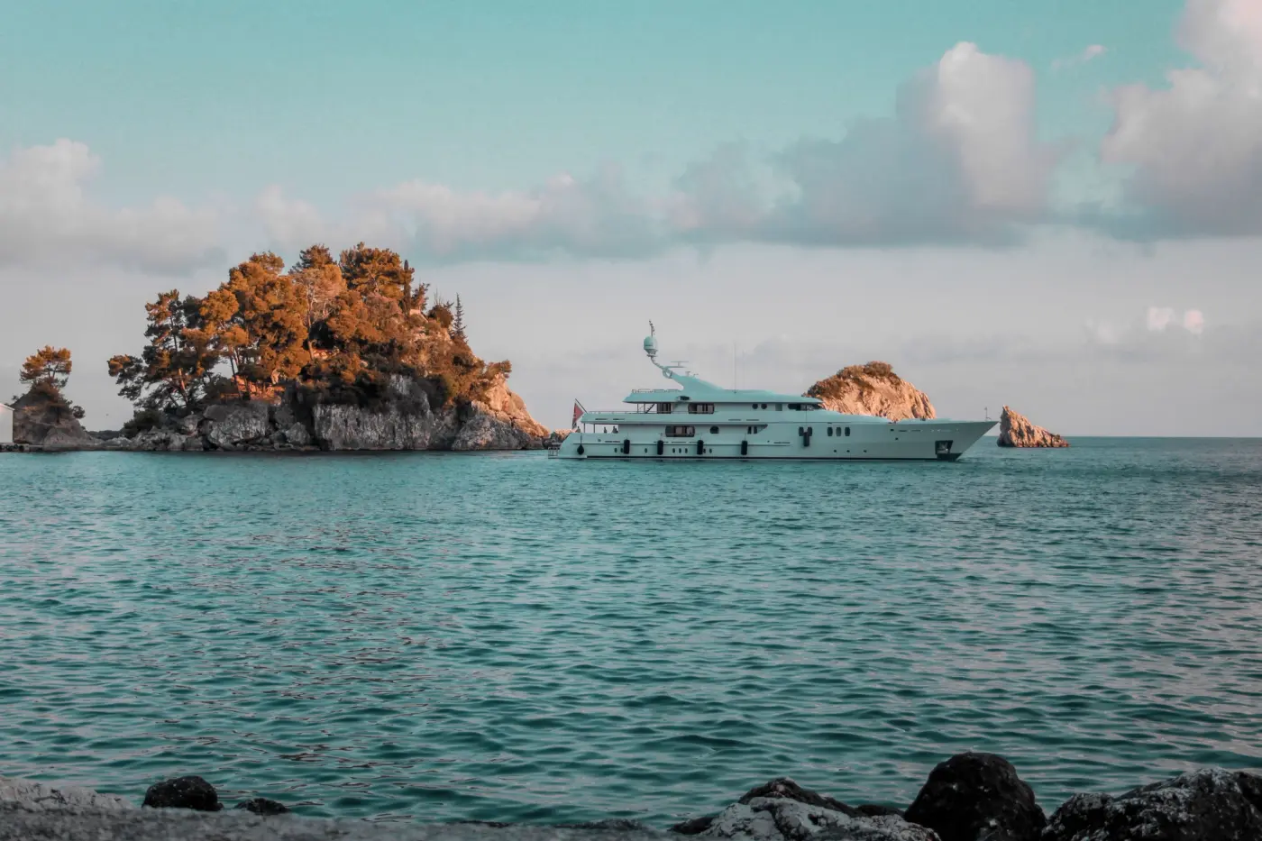 Crewed charter yacht at anchor in a calm Greek bay with tender and water toys aboard, all covered under the owner's policy