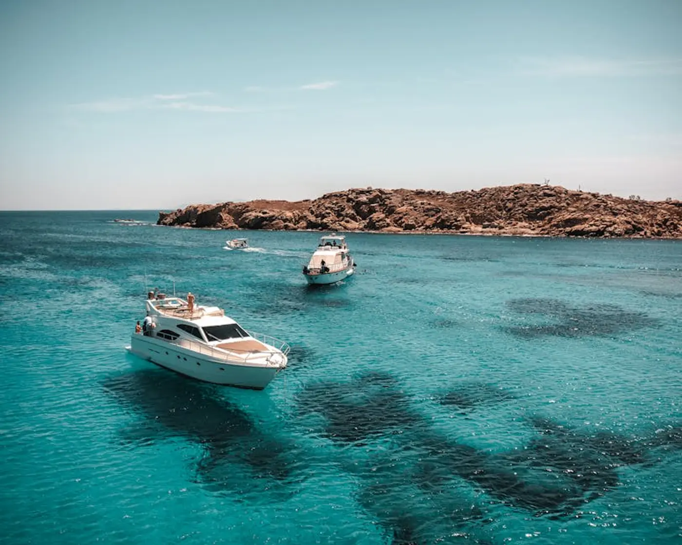 Aerial view of luxury yachts cruising crystal-clear blue waters near Mykonos, Greece — private yacht charter 2026