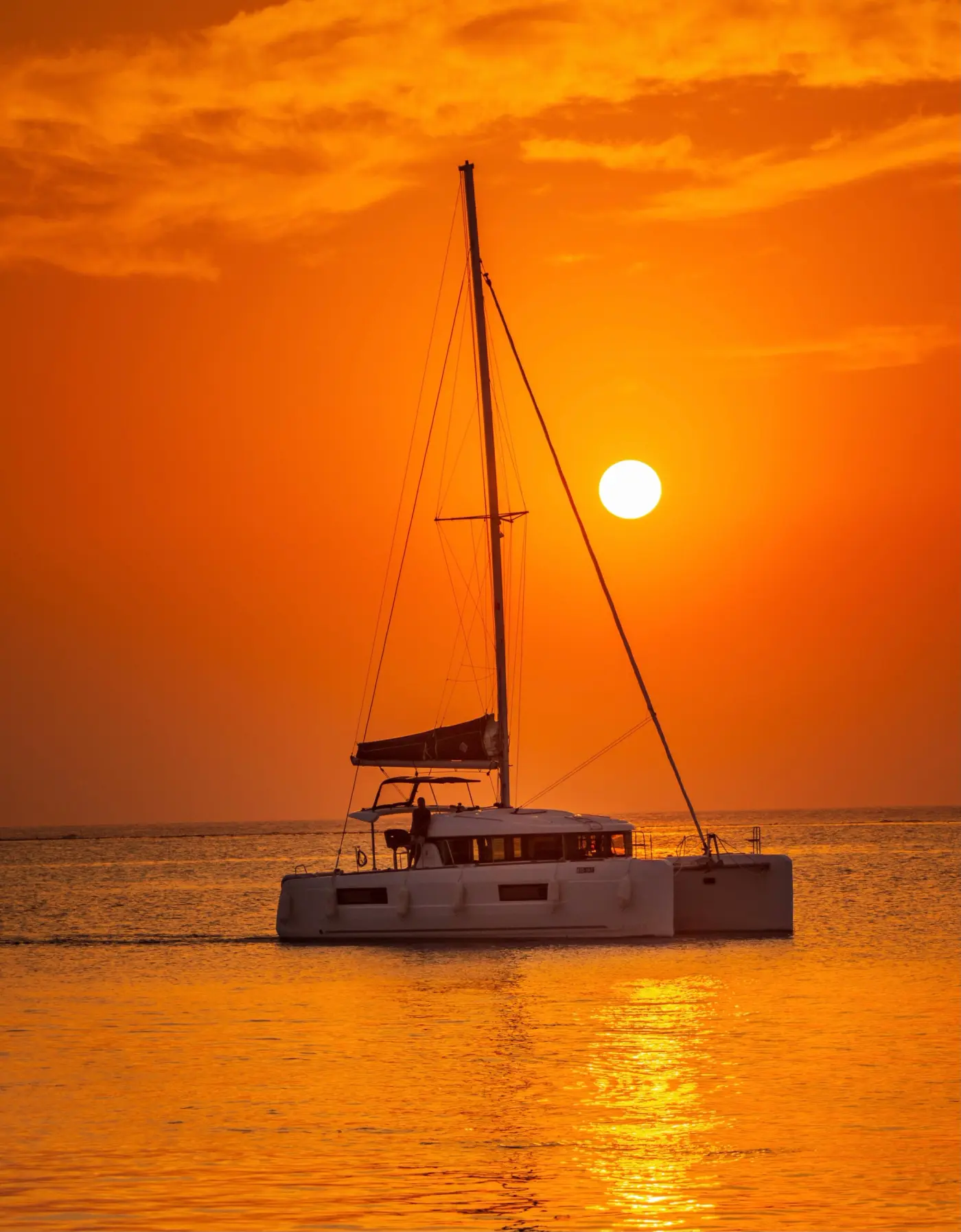 Crewed catamaran anchored alone in a turquoise Cycladic bay at golden hour, the setting of a Greek honeymoon charter