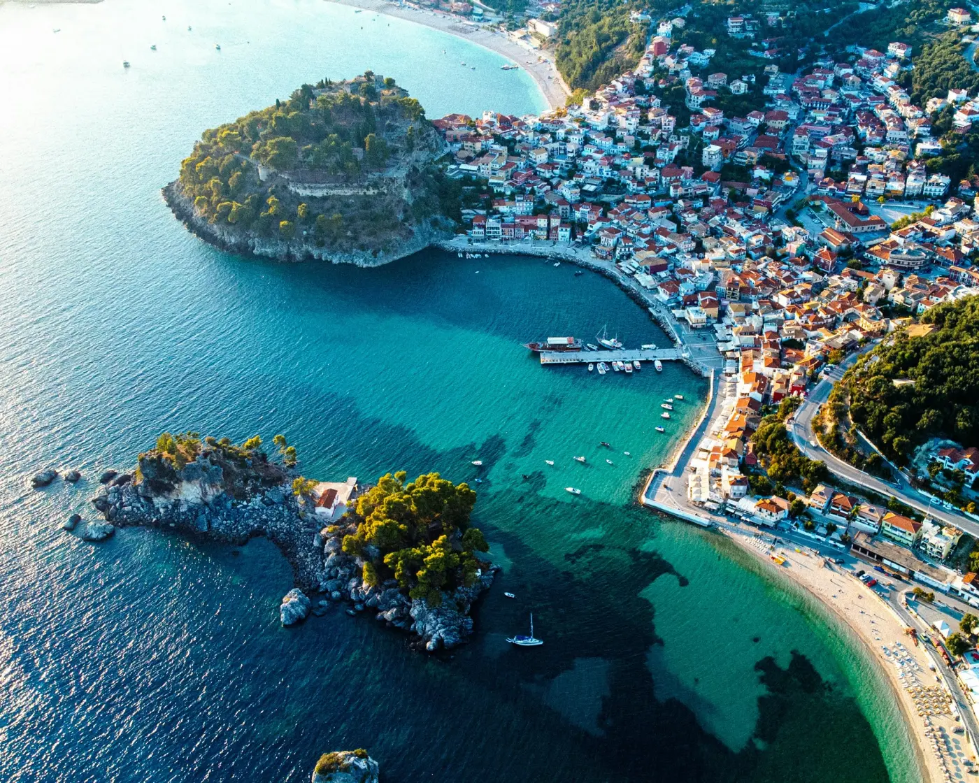 Aerial view of a Greek coastal town with turquoise waters and boats — yacht charter cost guide