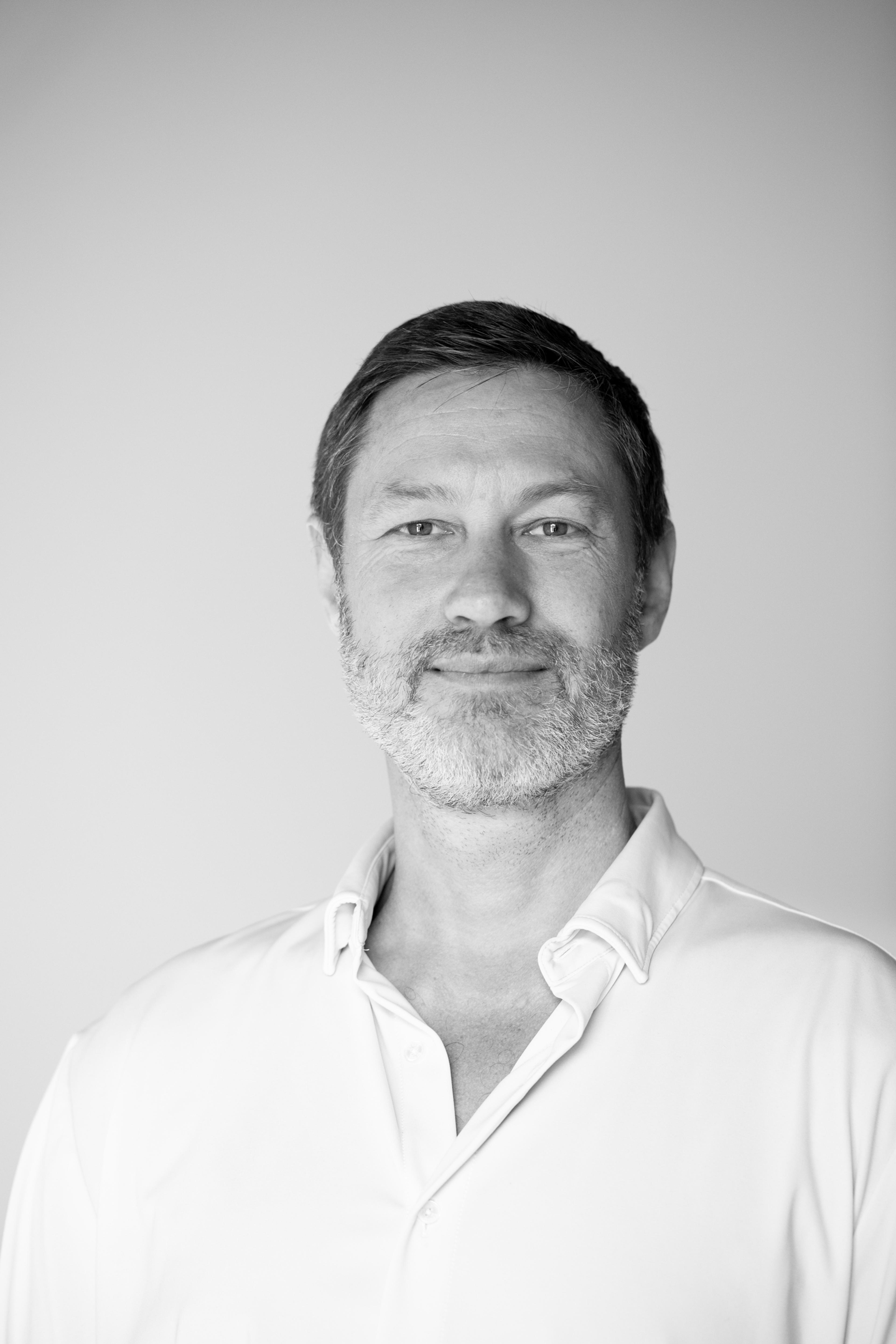 Black and white formal portrait of Dr. Lowan Stewart in an open white shirt against a plain background