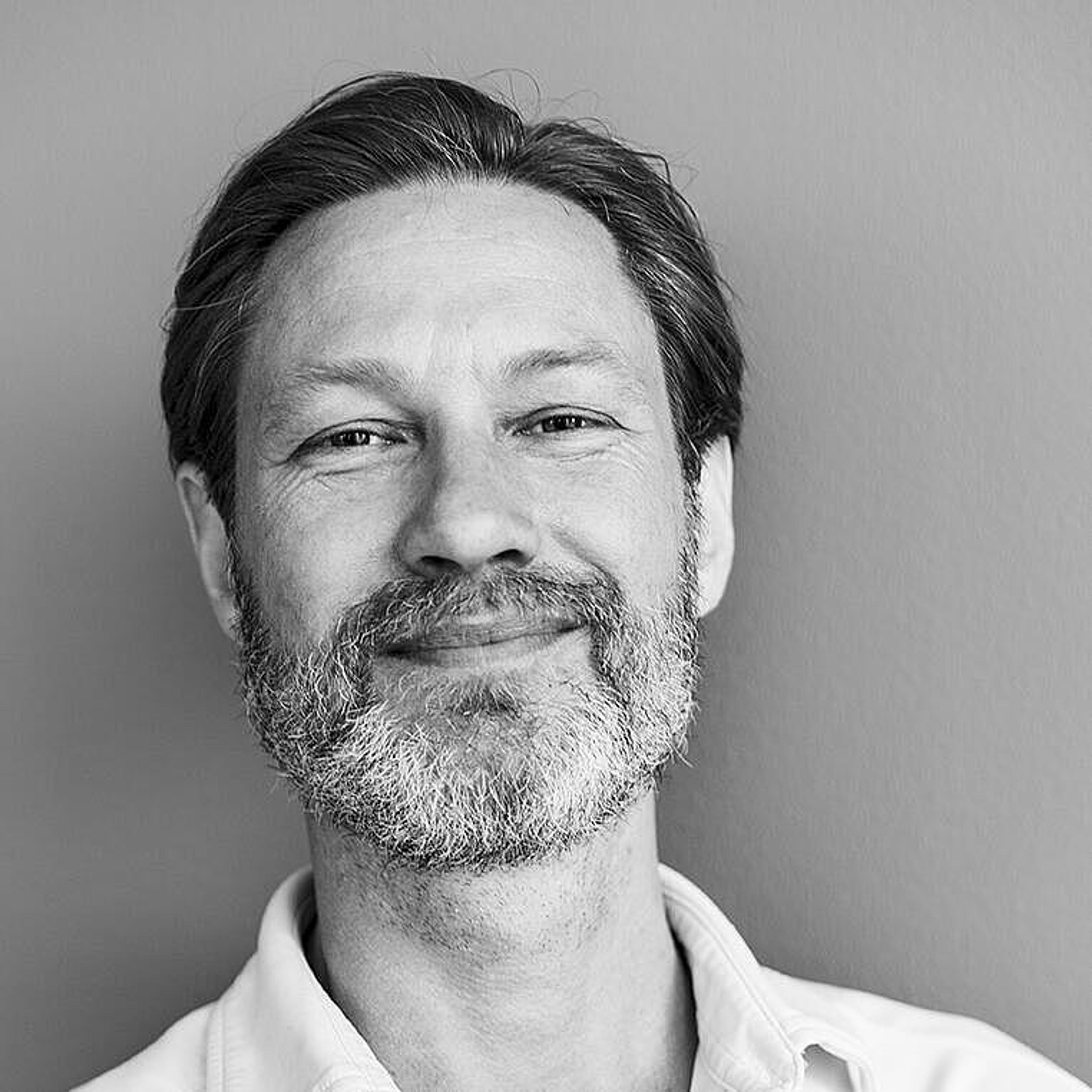 Black and white square headshot of Dr. Lowan Stewart smiling against a neutral background