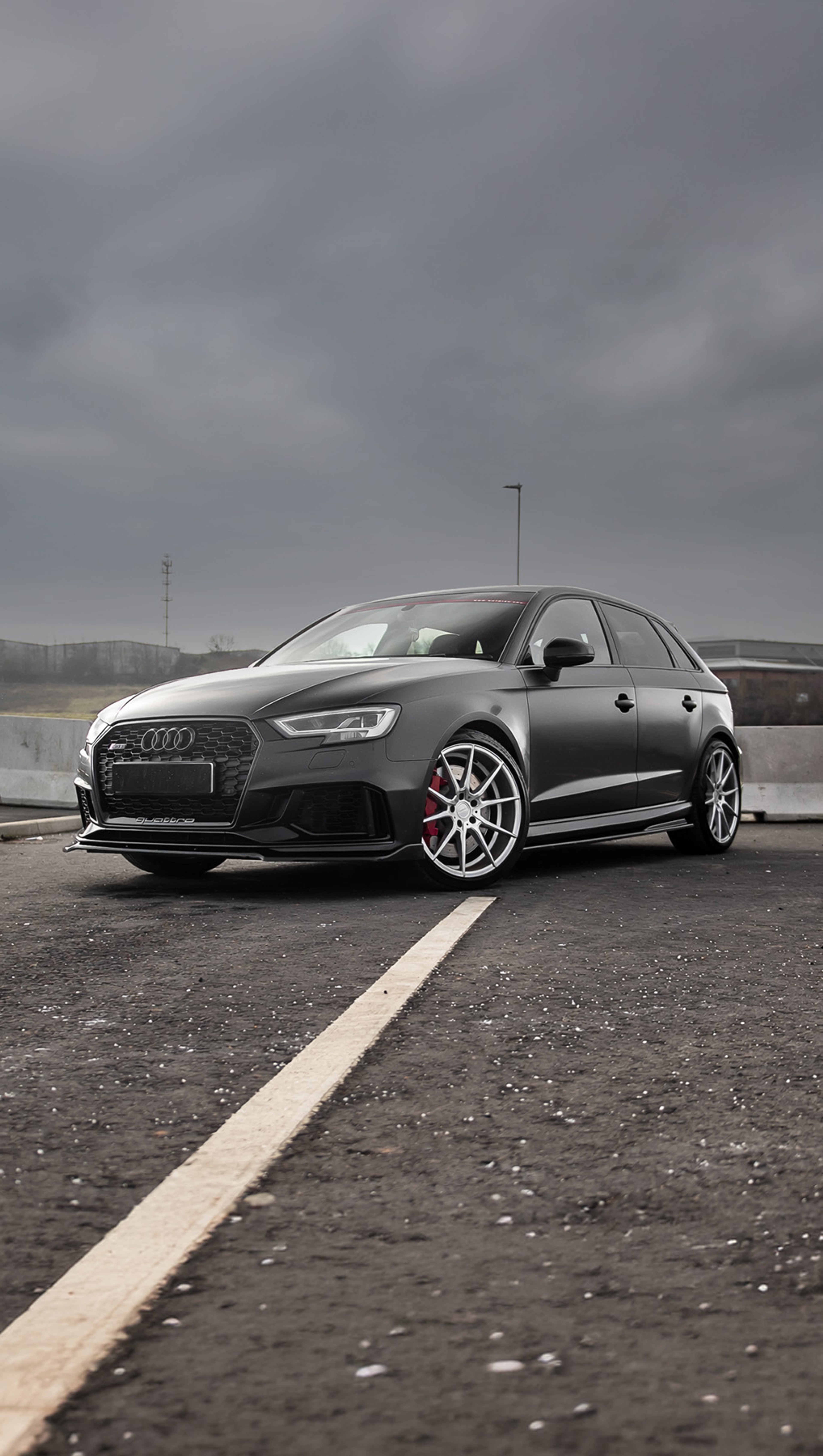 A custom Forge Audi RS3 in matte black sits parked on an asphalt lot under a cloudy, overcast sky.