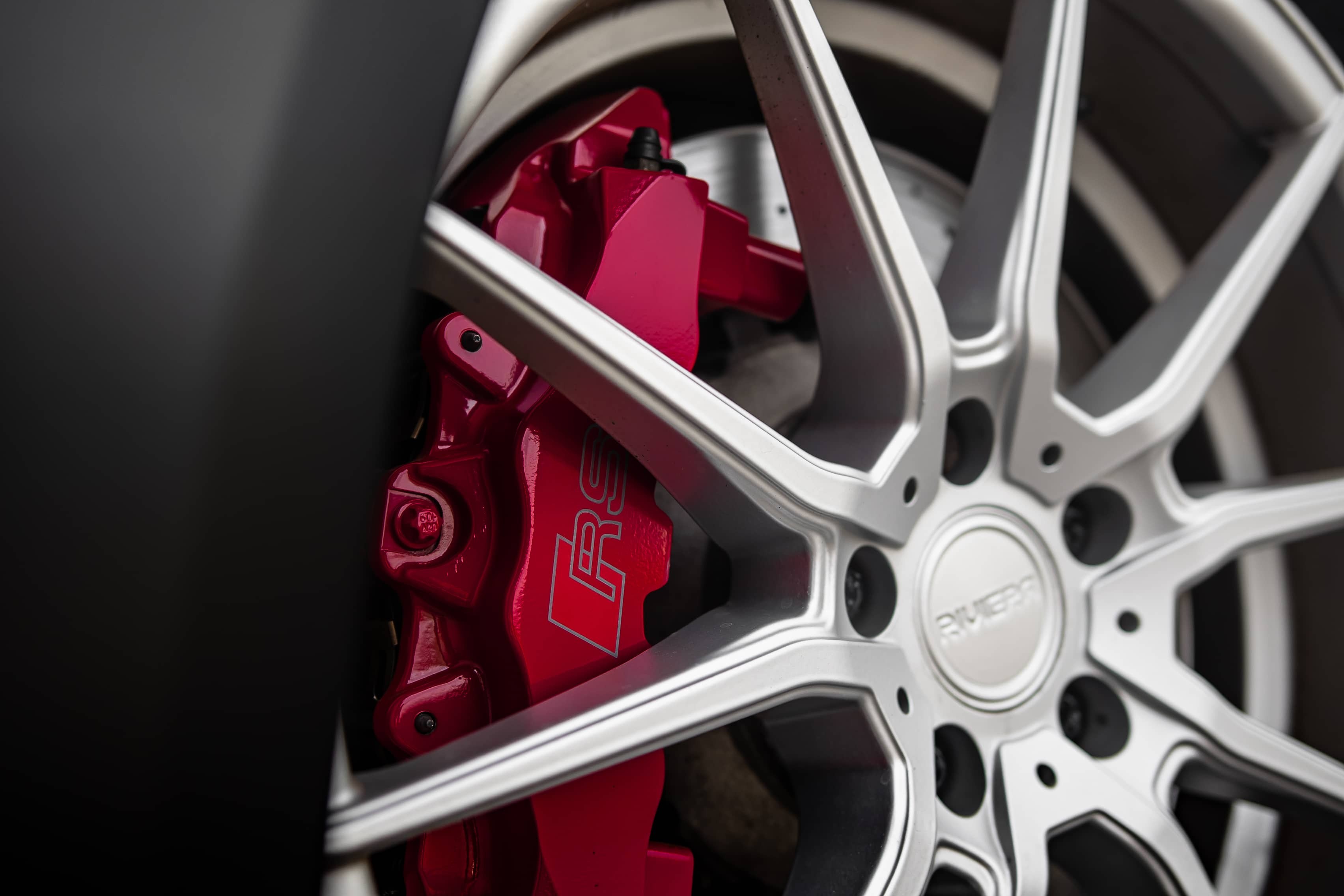 A close-up view shows a bright red RS brake caliper behind silver multi-spoke wheels on a custom Forge Audi RS3.