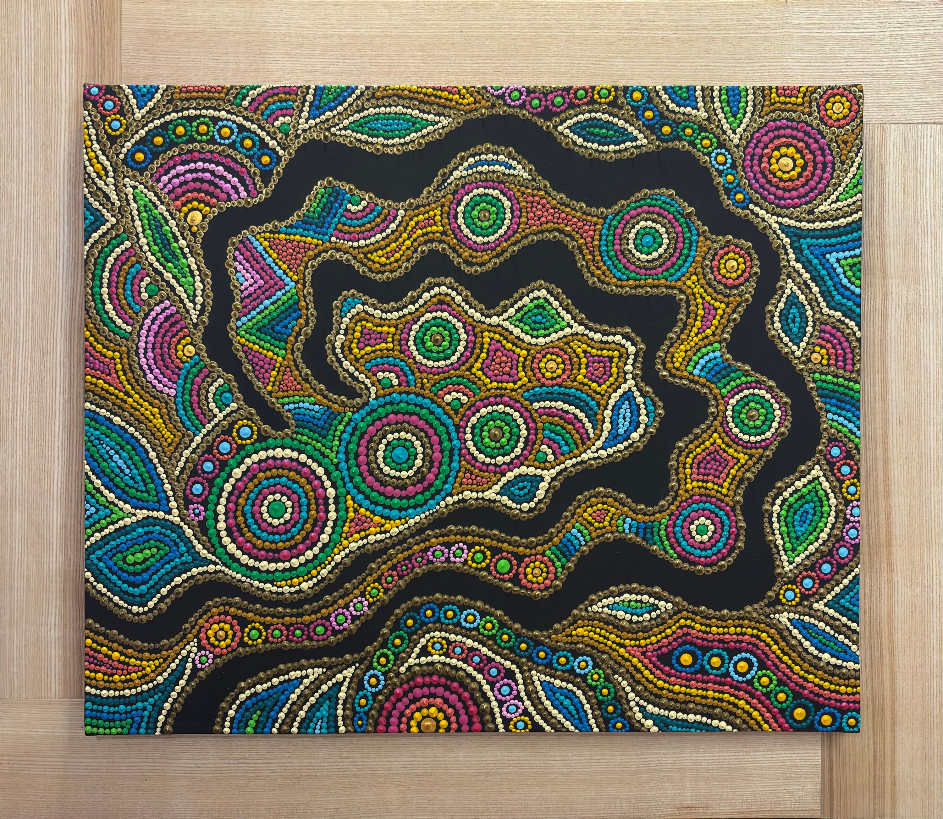 « Terre vibrante », Art aborigène contemporain de Caroline Pons. Toile aux motifs complexes de points vifs multicolores sur fond noir, encadrée de bois de frêne clair.