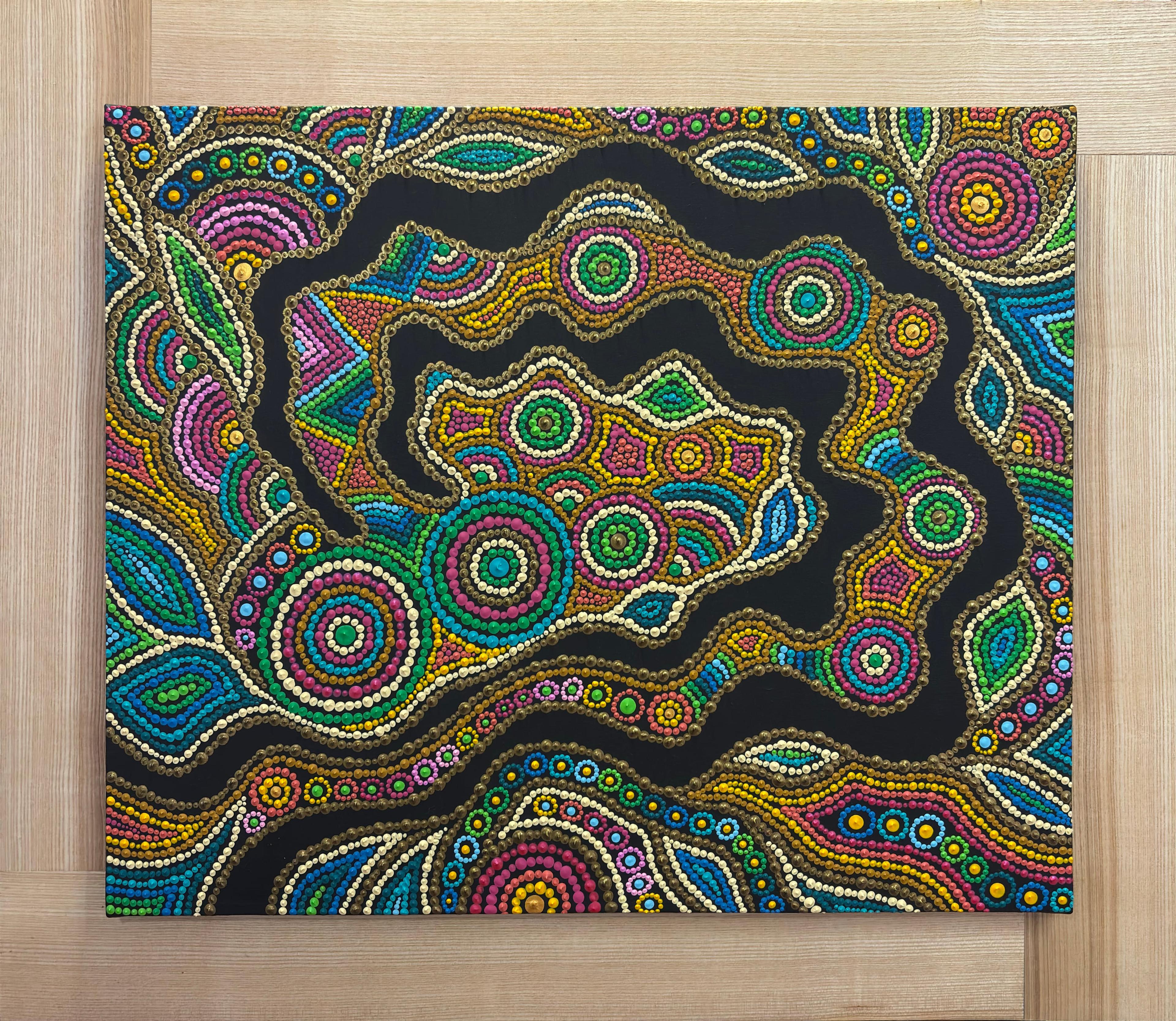 Caroline Pons' "Terre vibrante" art. Vivid contemporary aboriginal-style dot patterns in green, blue, pink, gold, white on black canvas, displayed on light wood.