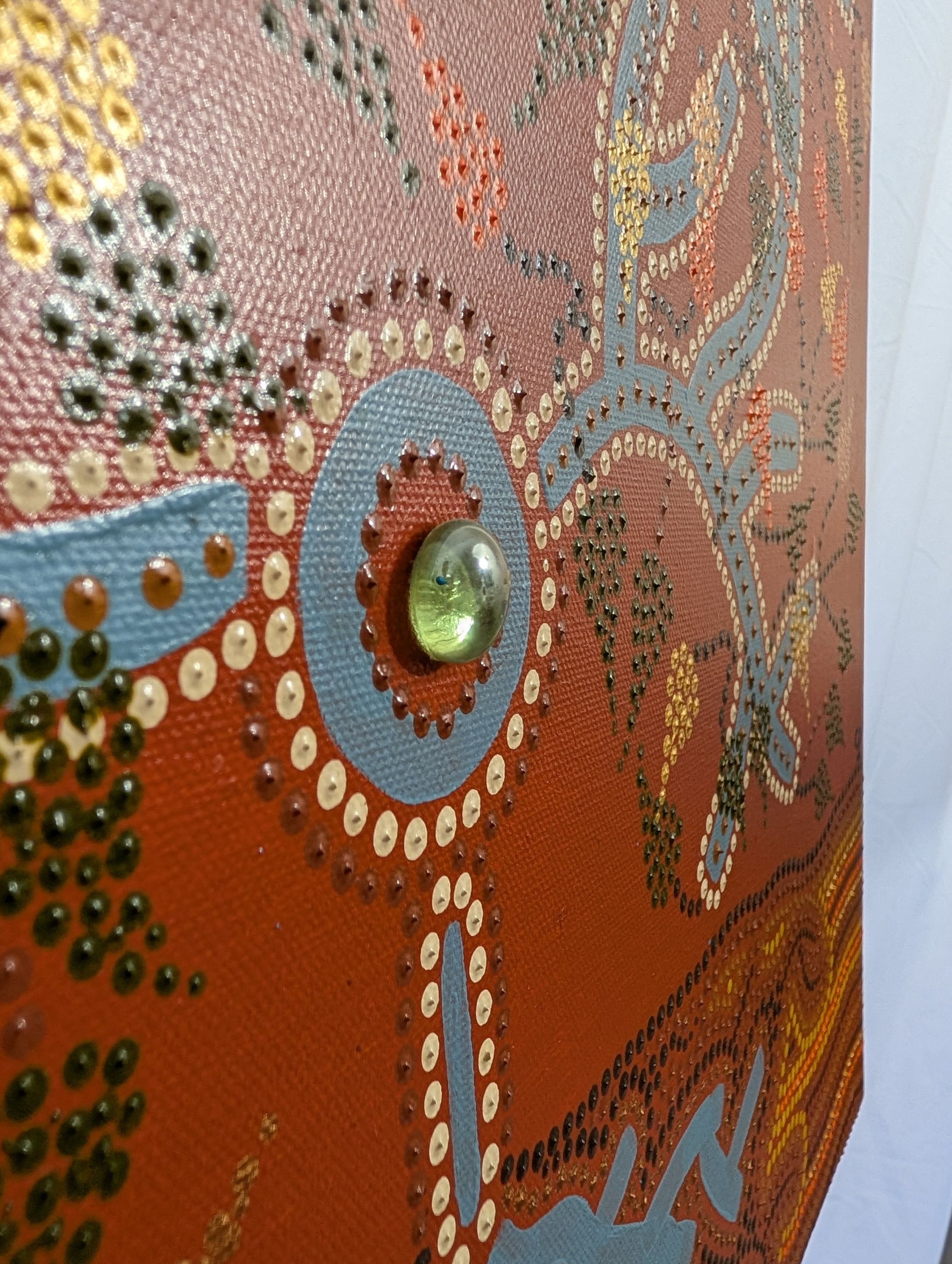 Close-up of "L'arbre", contemporary aboriginal-style art by Caroline Pons, showcasing the tactile dot texture in orange, blue, gold, and the embedded green glass marble.