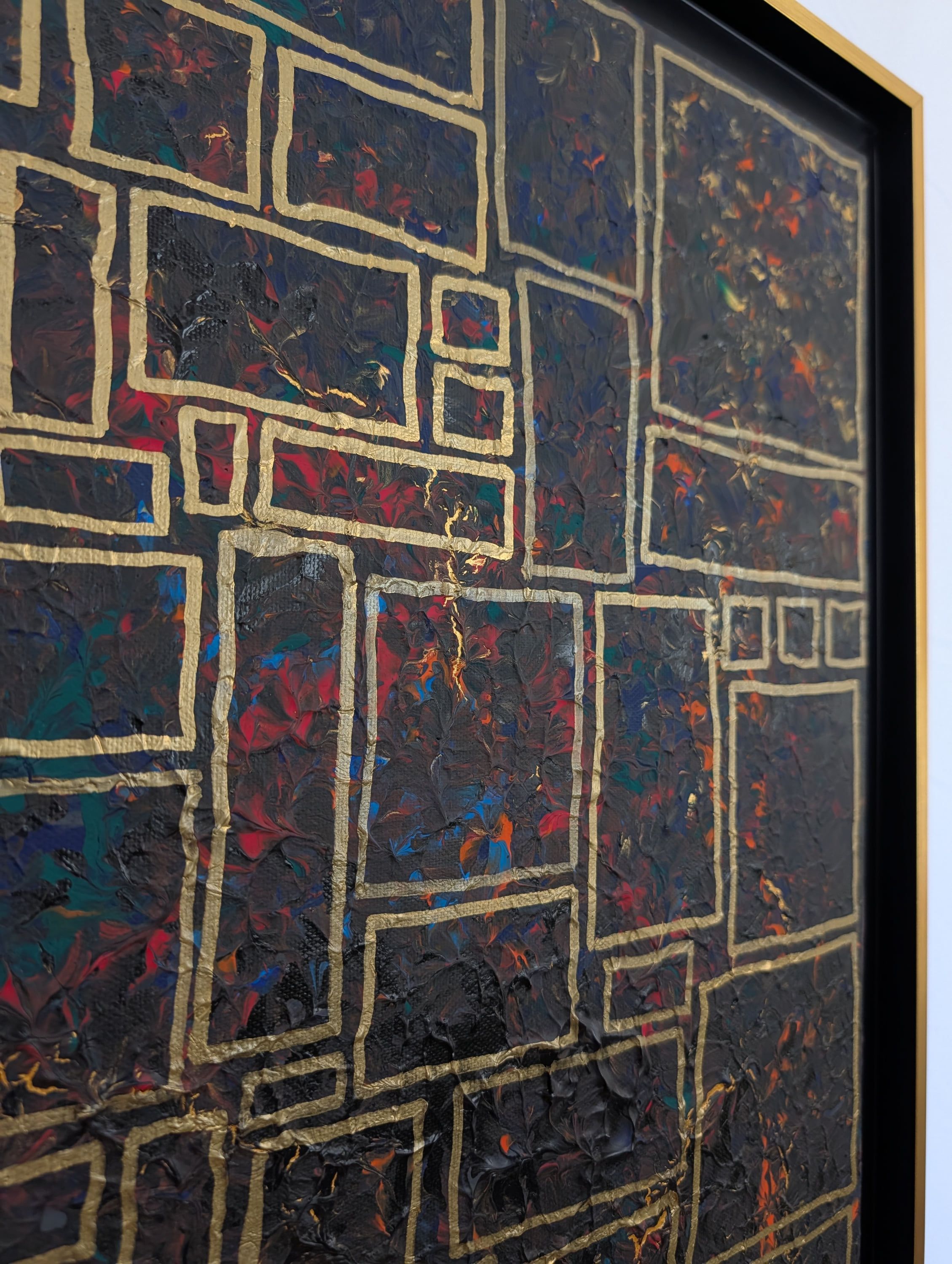 Détail de "La ville enfouie" par Caroline Pons, un tableau abstrait contemporain. Texture riche et sombre (rouge, orange, bleu, noir) avec des motifs rectangulaires dorés, encadré.