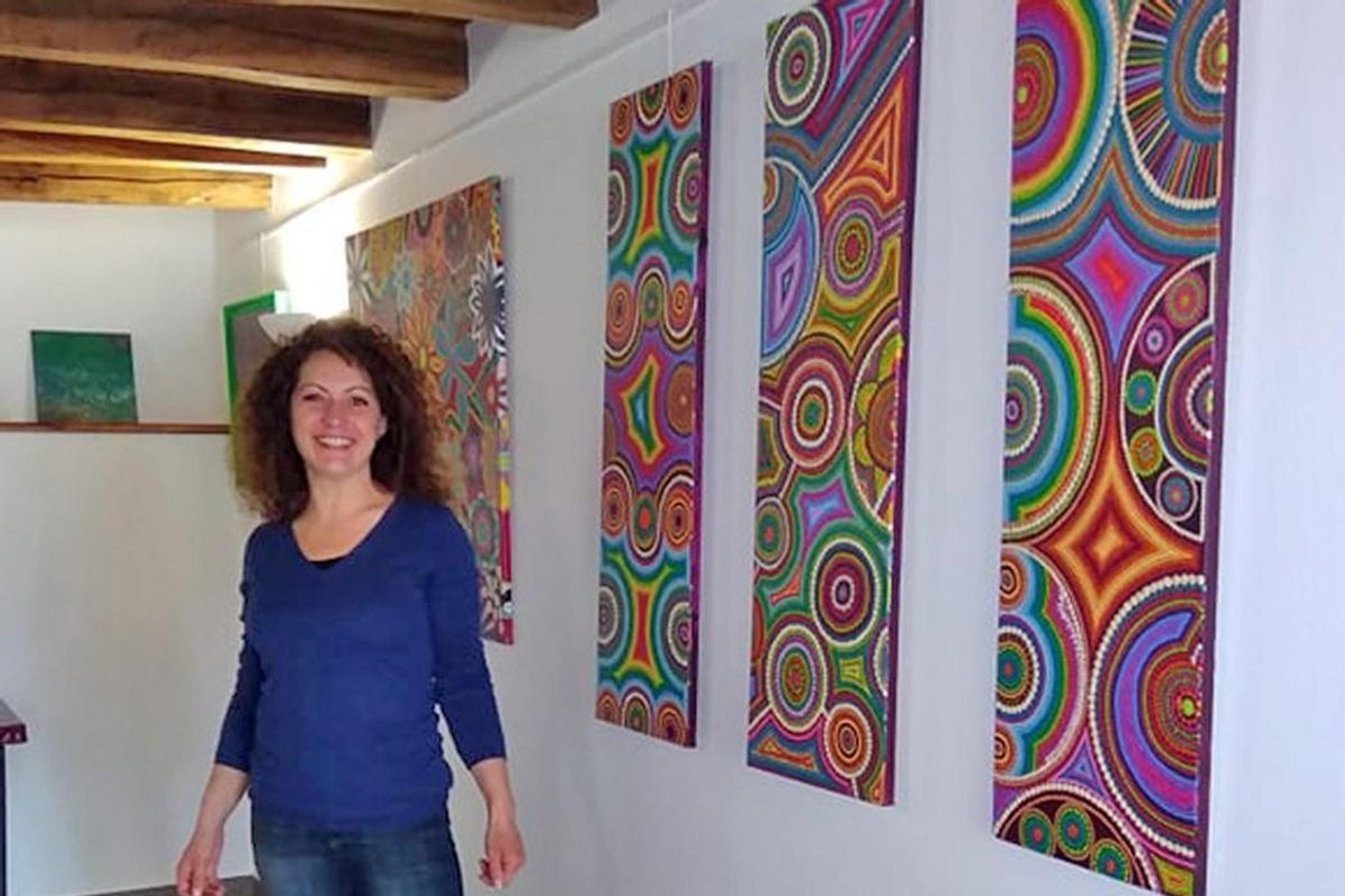 Caroline Pons beside three tall canvases of coloured dots