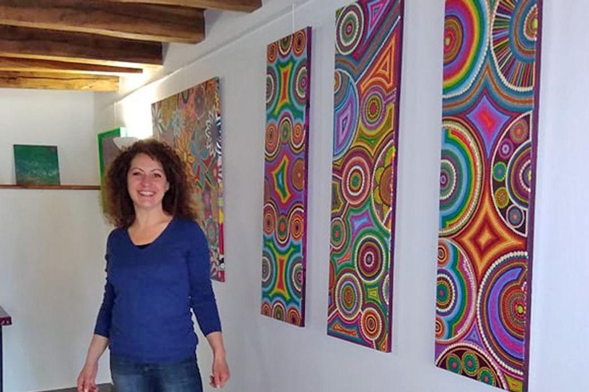 Caroline Pons beside three tall canvases of coloured dots