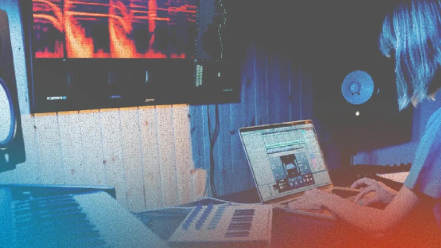 A person producing music at a home studio setup with a laptop, MIDI keyboard, and studio monitors