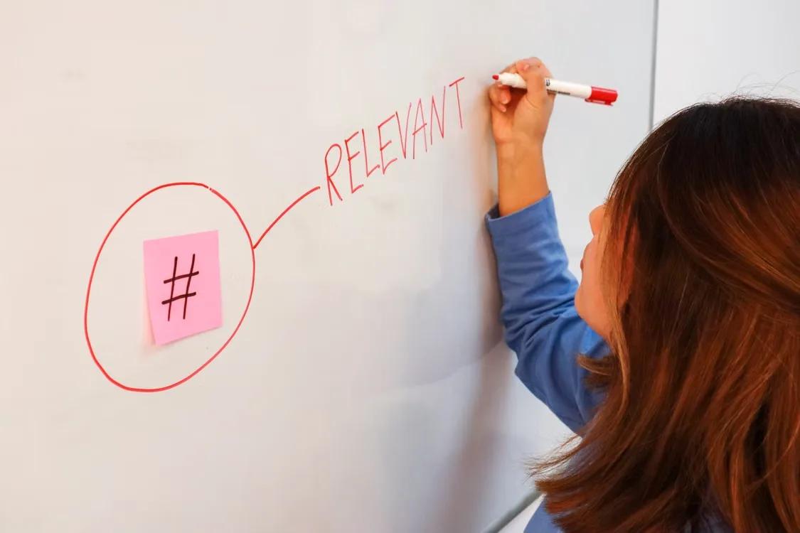 A person writing the word "relevant" on a whiteboard next to a circled sticky note