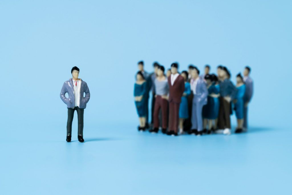 A single miniature figure standing apart from a crowd of similar figures on a blue background