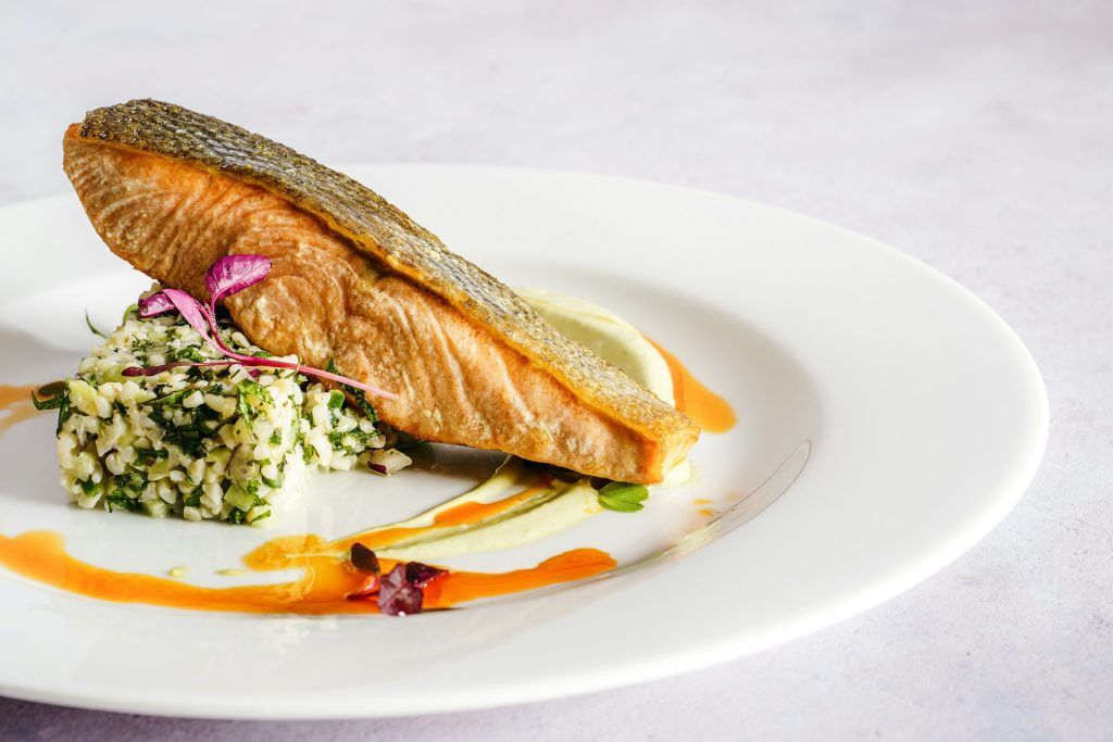 A plated fillet of seared fish with herbed rice and a citrus sauce garnish