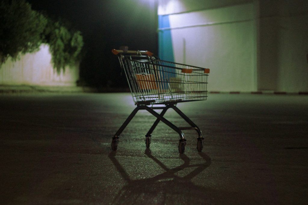 An empty shopping cart alone in a dimly lit parking lot at night