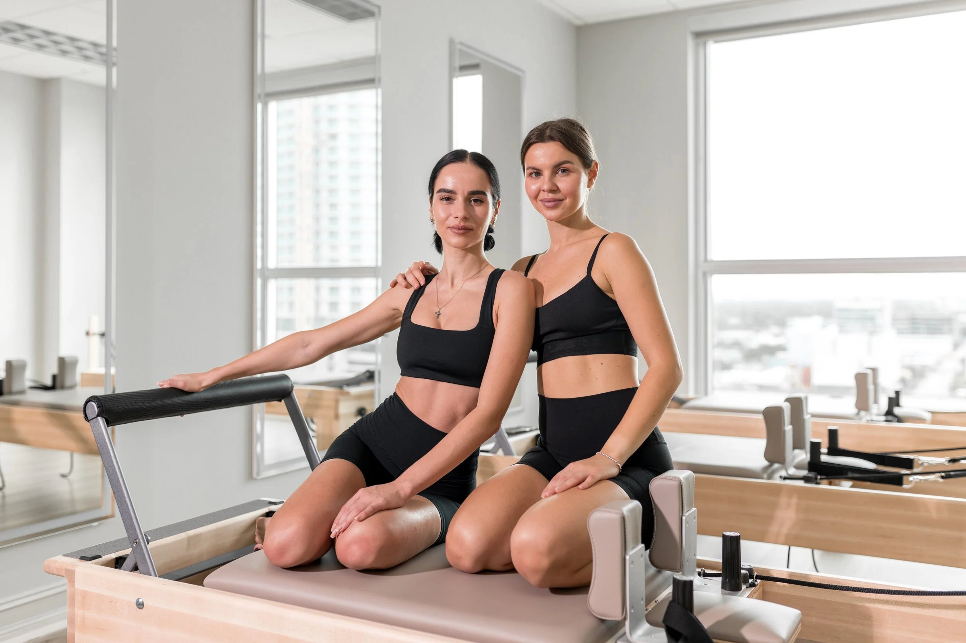 Two people seated on reformers in Kinona Studio's sunlit Brickell space.