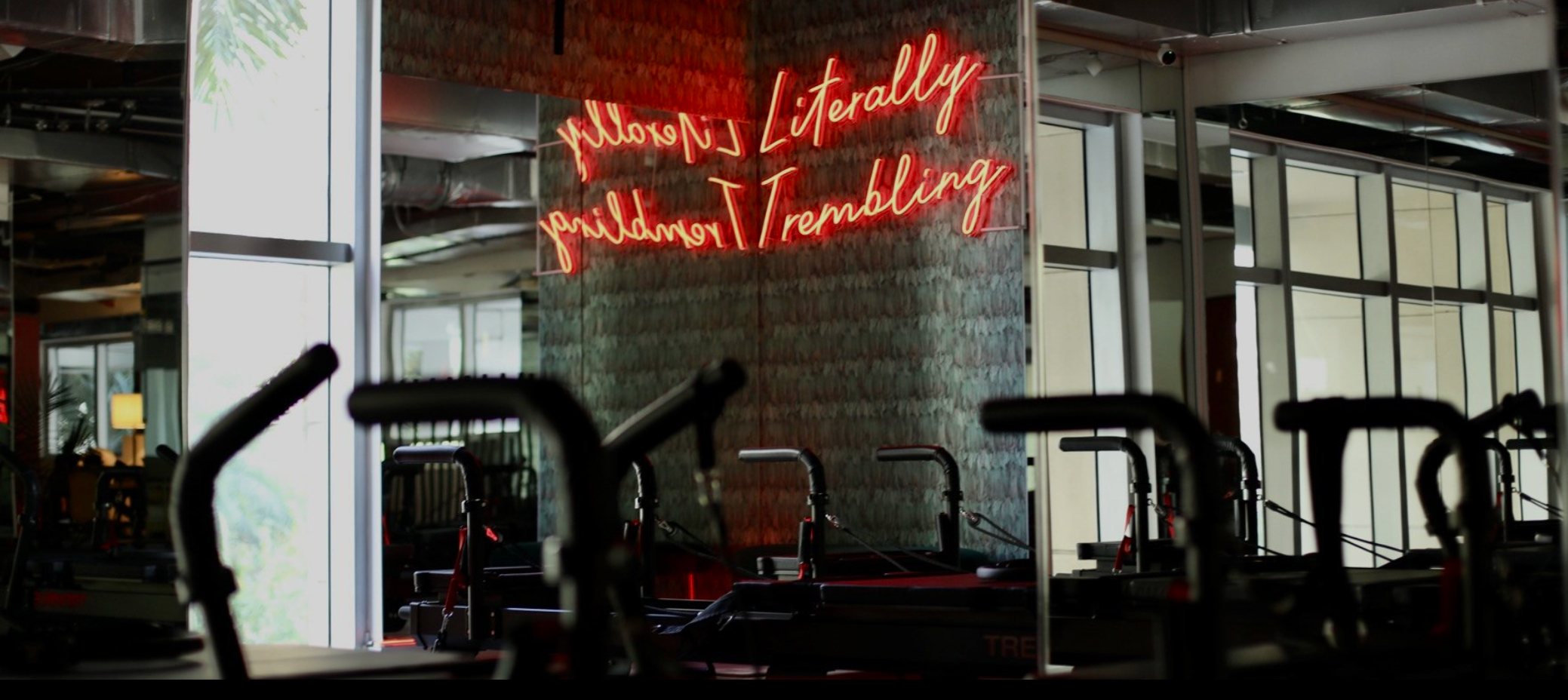 Reformer machines and a neon wall sign inside TREMBLE Brickell.