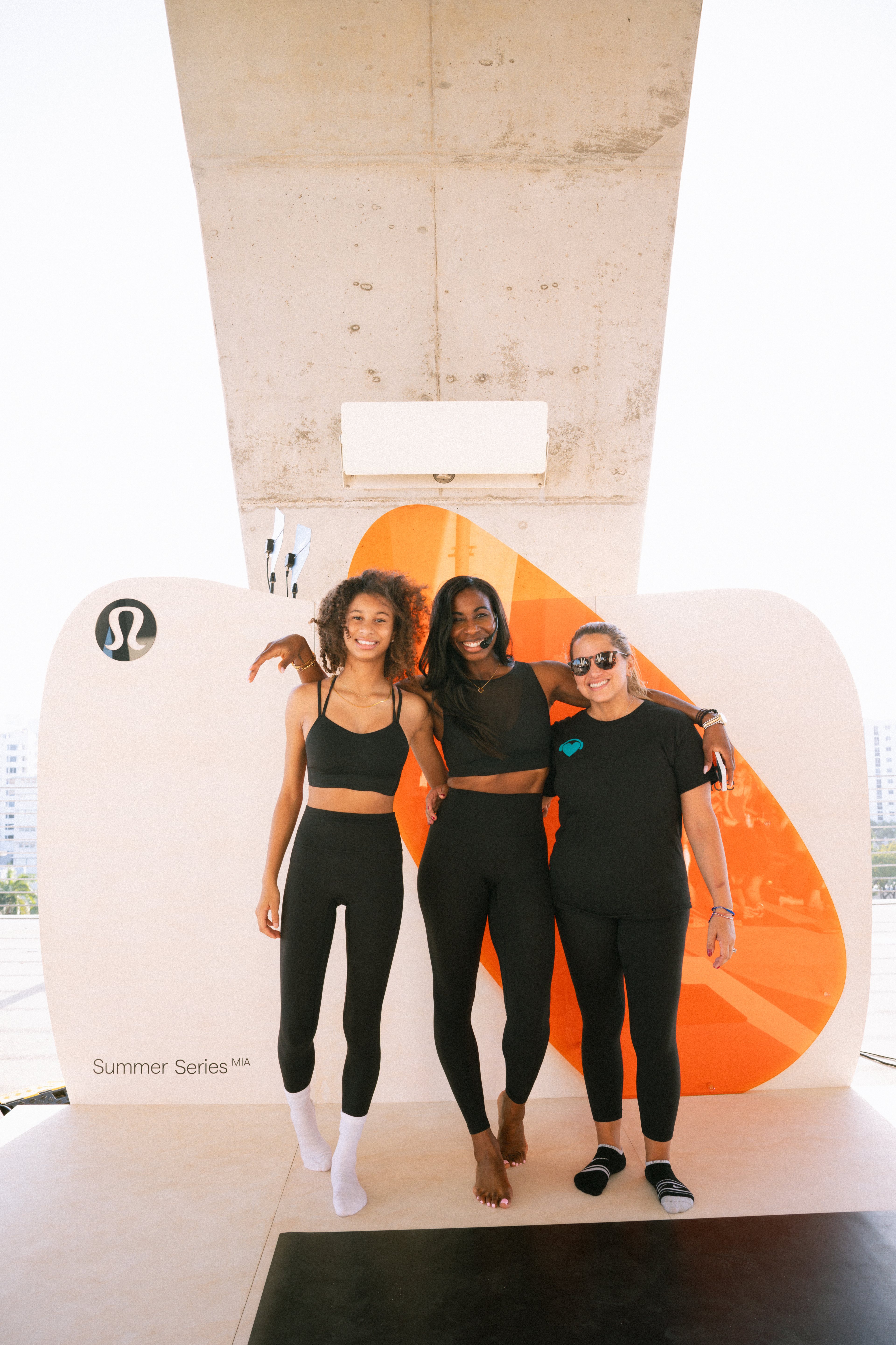 Three people pose in front of the white-and-orange lululemon backdrop at 1111 Lincoln Road.
