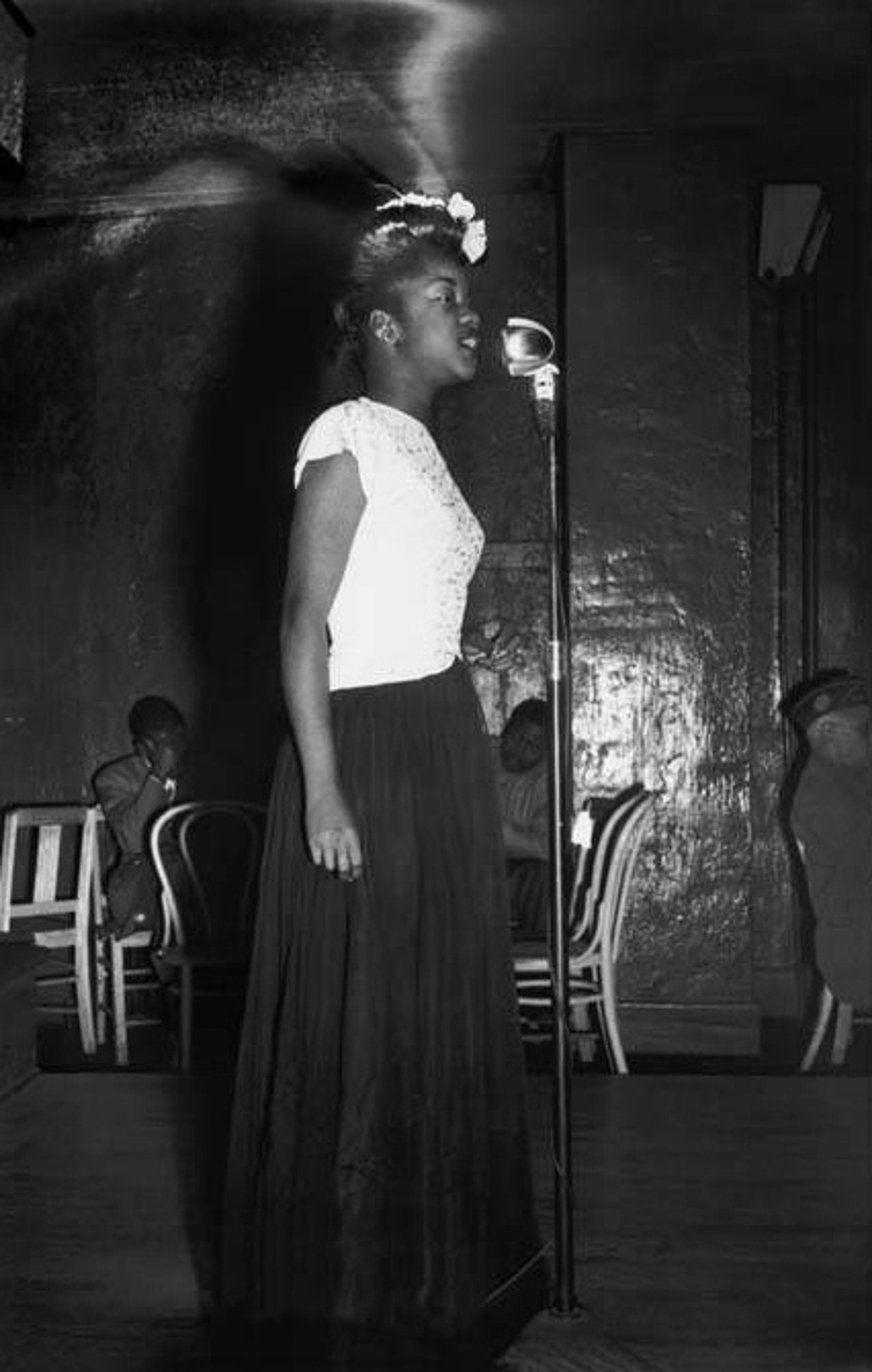 Person in long skirt singing in front of a mic, black and white photo