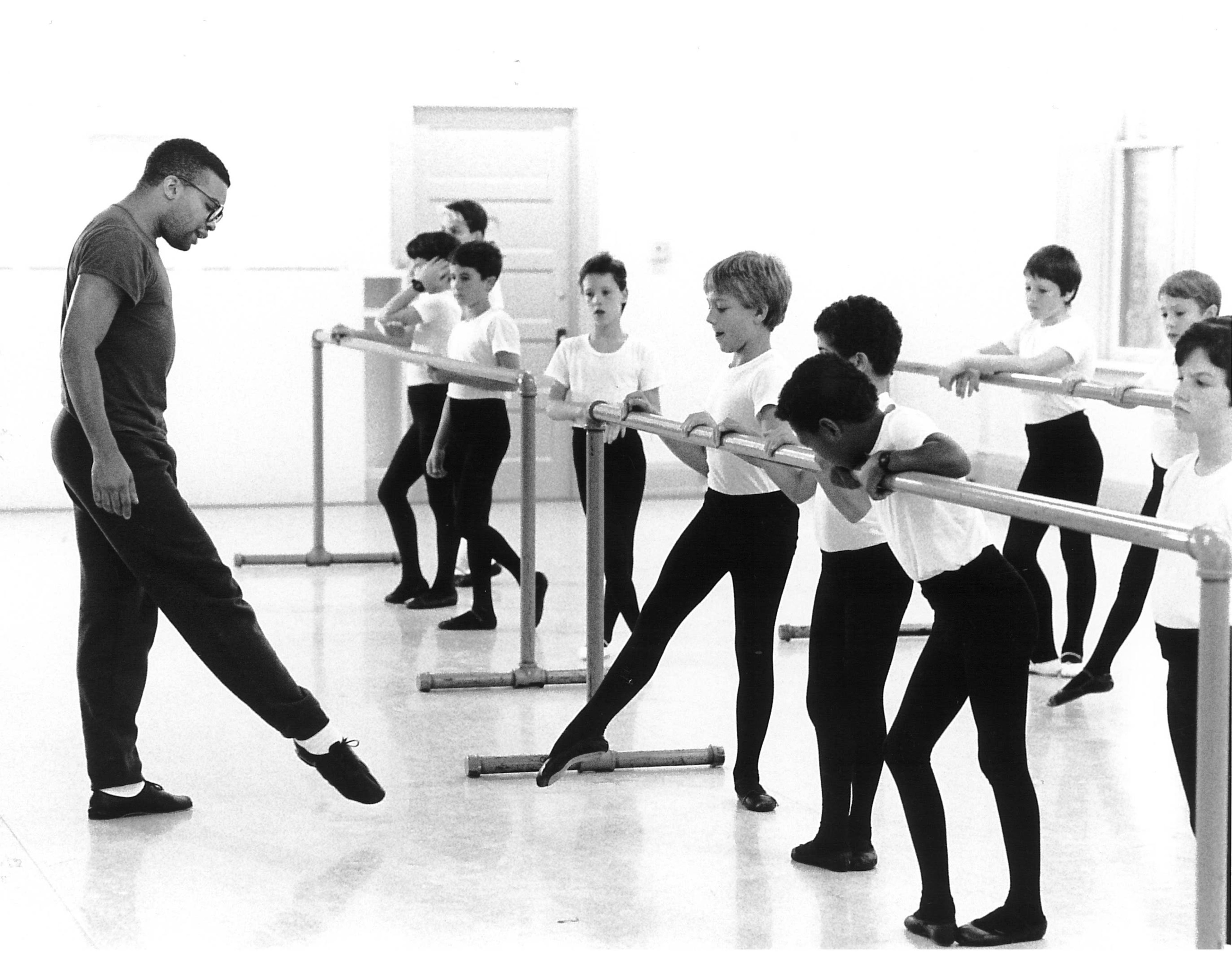 black and white photo of person teaching kids at the barre a ballet pose