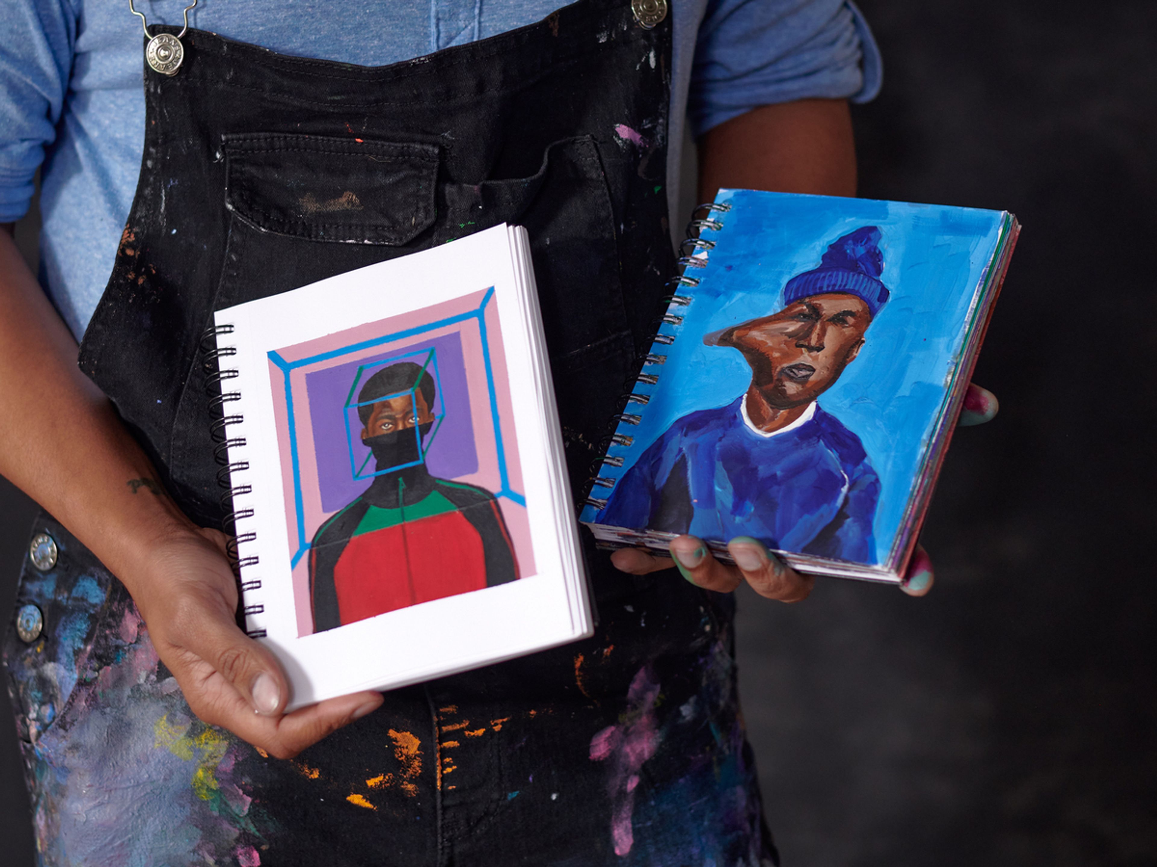 person holding two note books with paintings in them