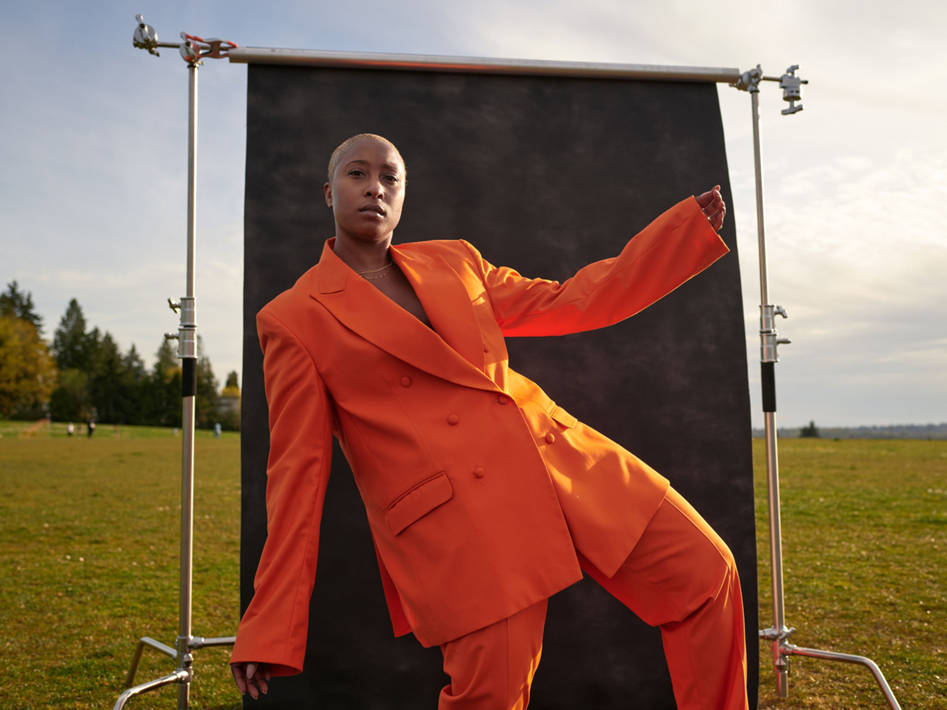 Person in orange oversized suit dancing in front of a black screen