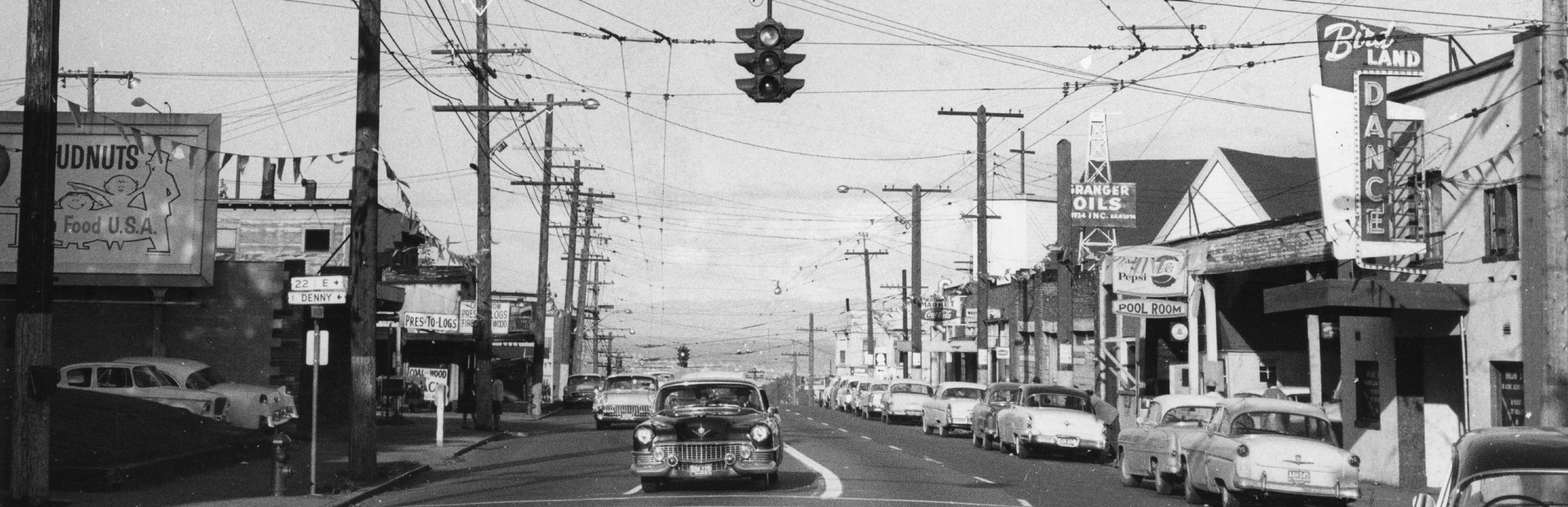 black and white image of a street with cars and power lines overhead 