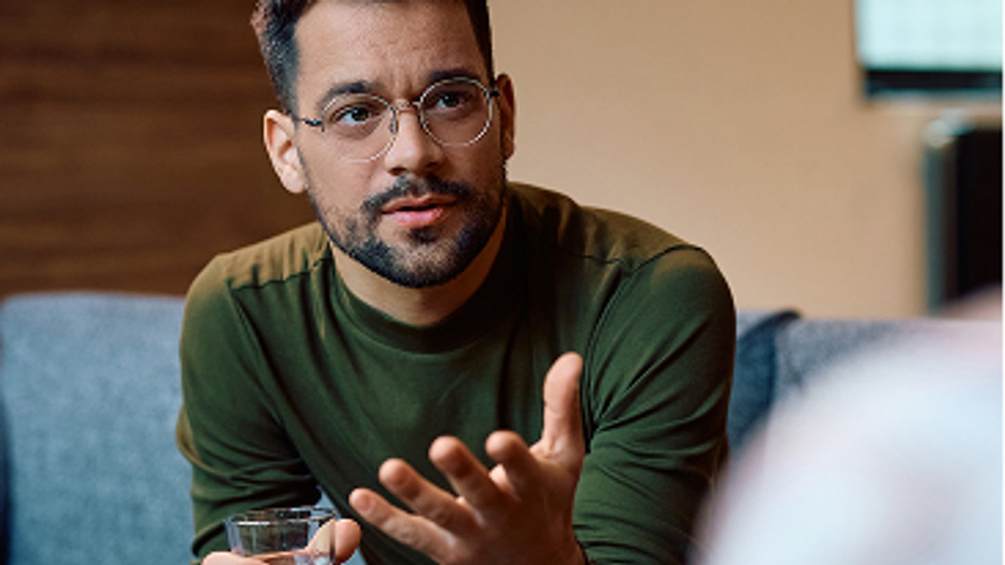 A man holding a glass of water during a conversation