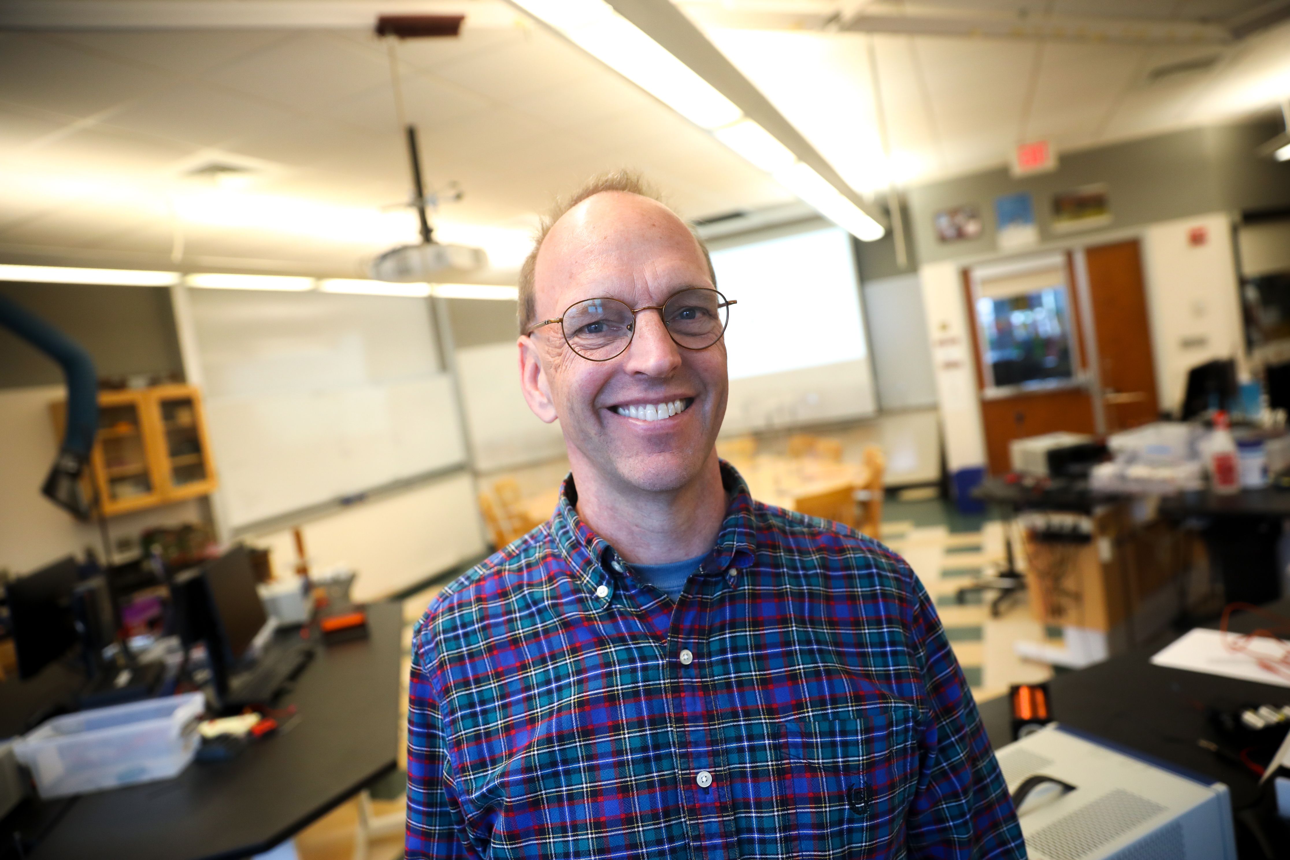 A teacher stands in his classroom and grins.