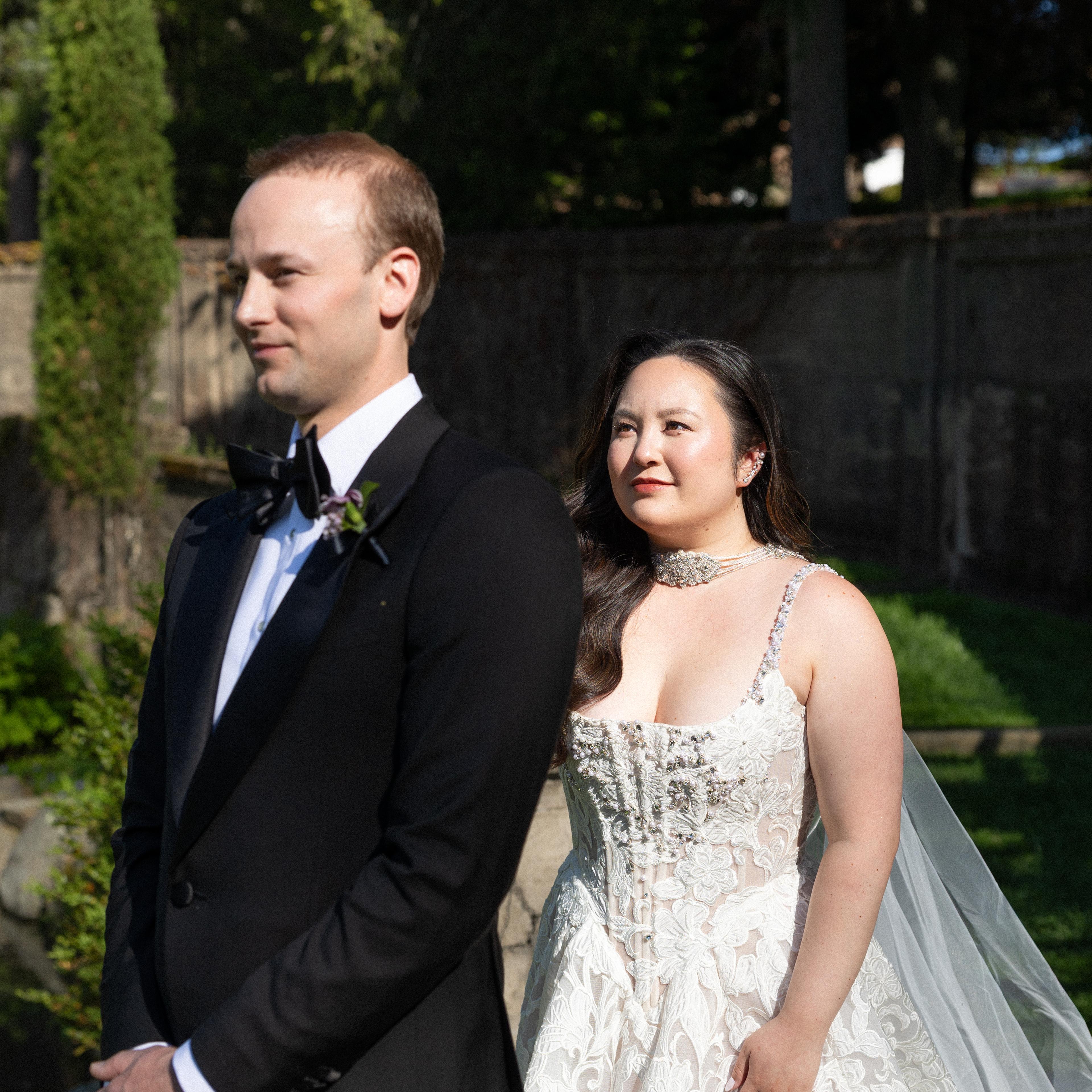 Groom stands in a tux as bride walks behind in a wedding dress